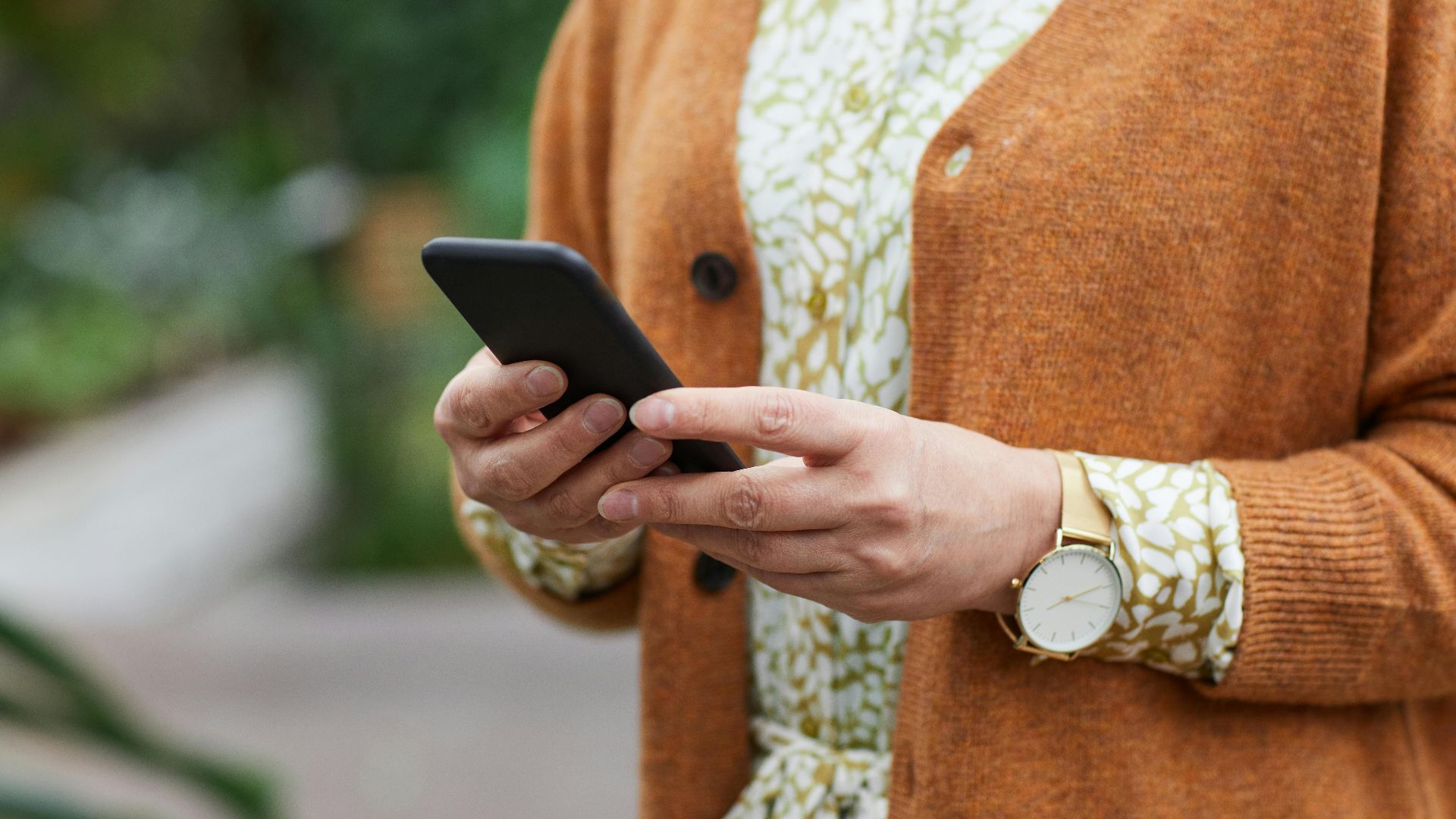 Elderly person's hands holding a smartphone in a casual setting, wearing a watch.