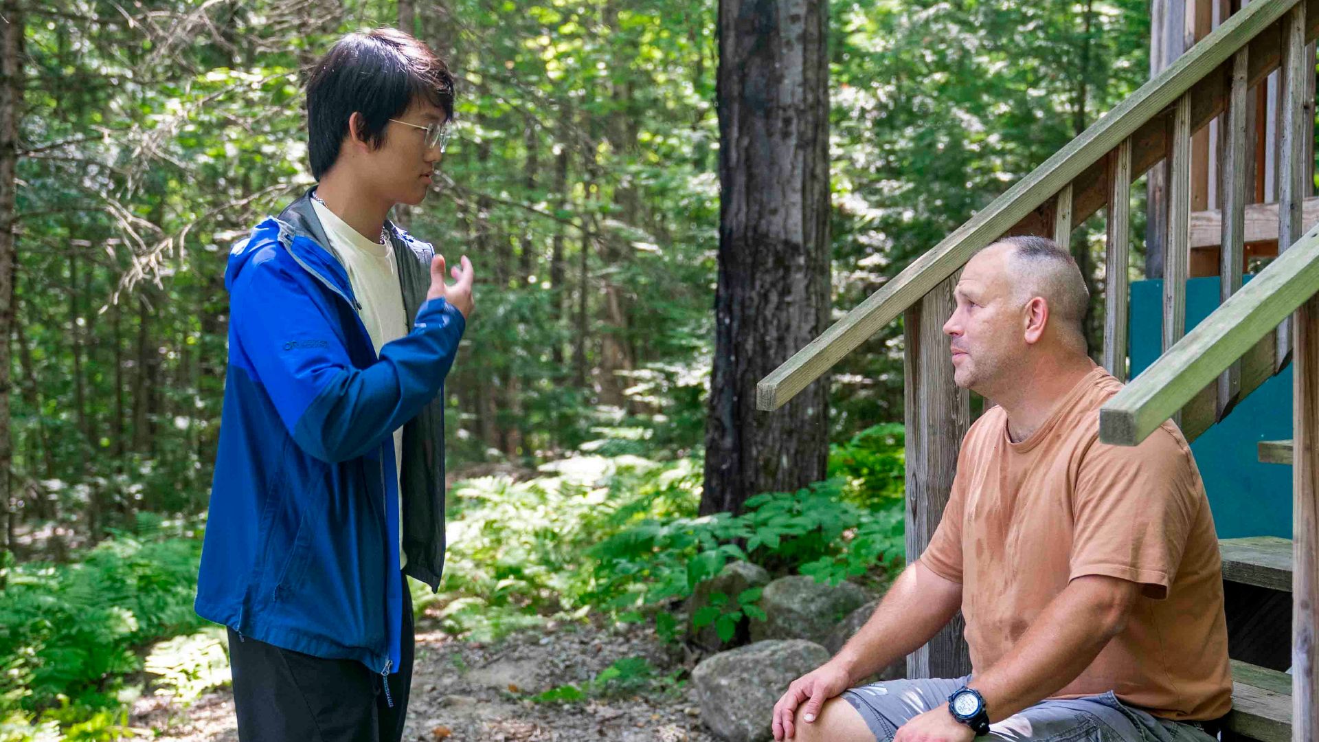 Two men talking outside a cabin in the woods