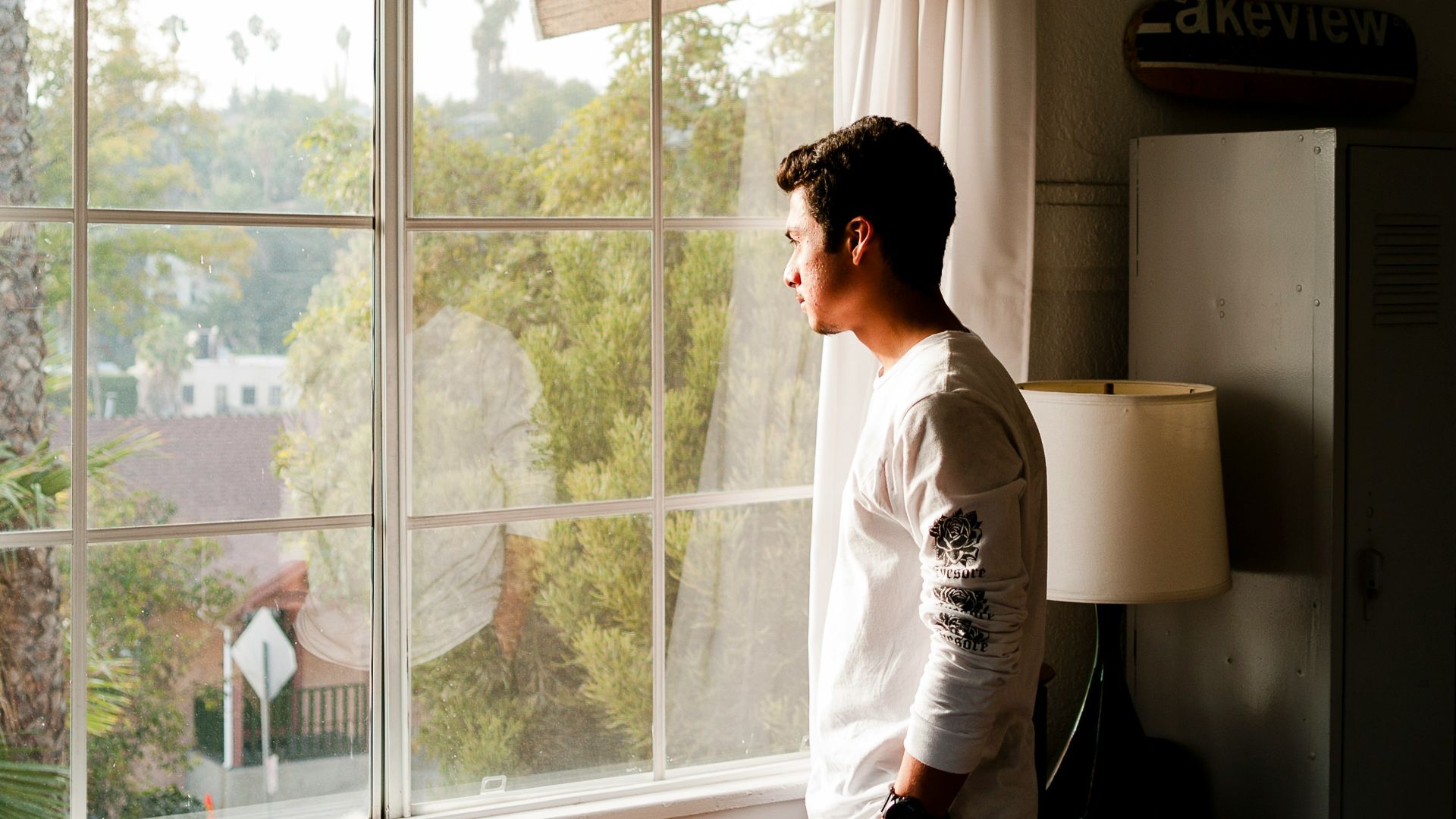 man wearing gray and black crew-neck shirt standing and looking out window