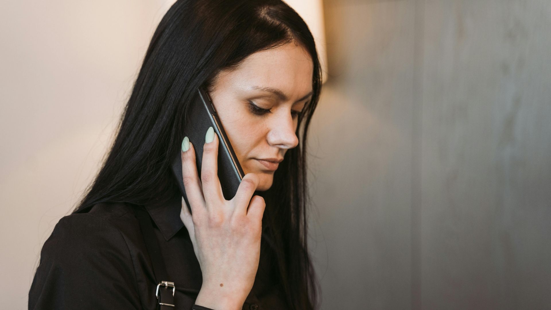 Side view of a woman with long hair holding a mobile phone, engaged in conversation.