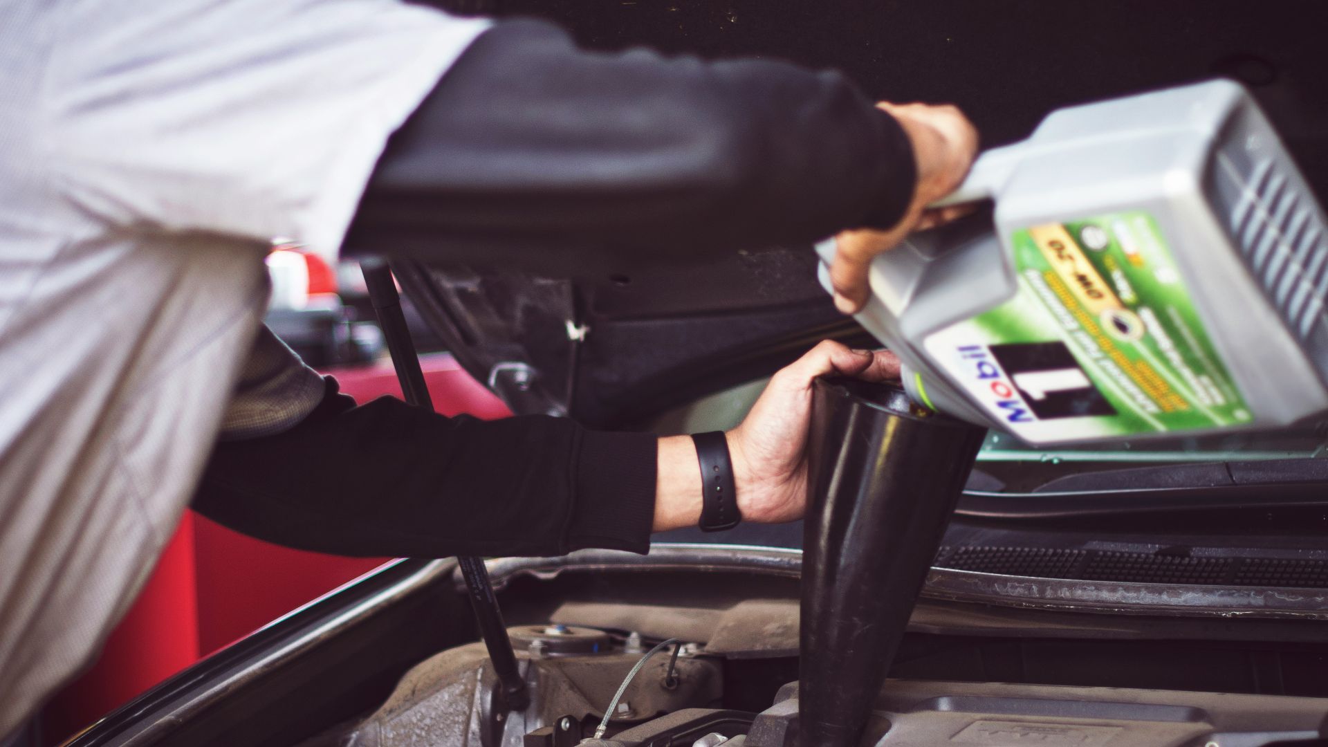 man refilling motor oil on car engine bay