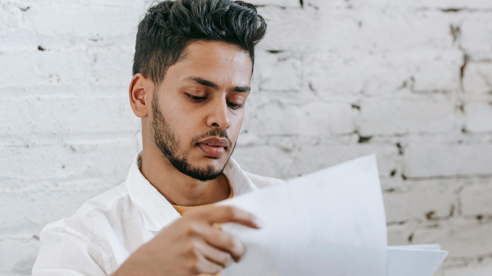 Concentrated young bearded Hispanic male sitting in armchair and analyzing contract while getting job offer