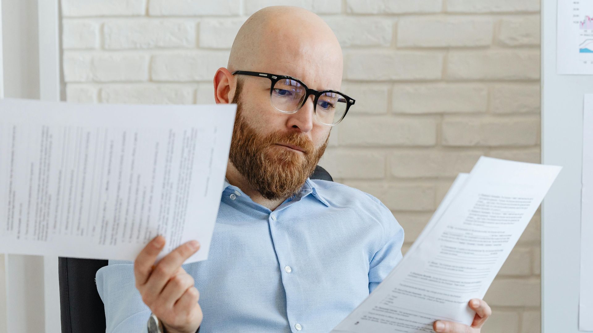 Bald bearded businessman reading financial documents in modern office setting.