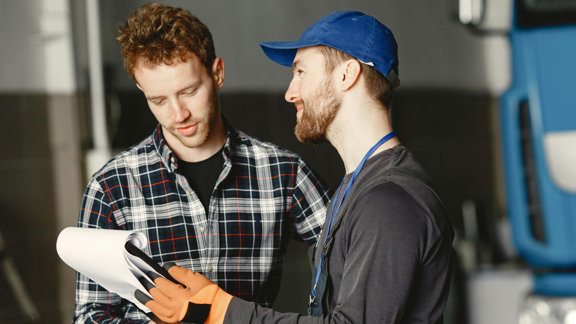Mechanic in uniform consults with customer in garage setting beside a blue truck.