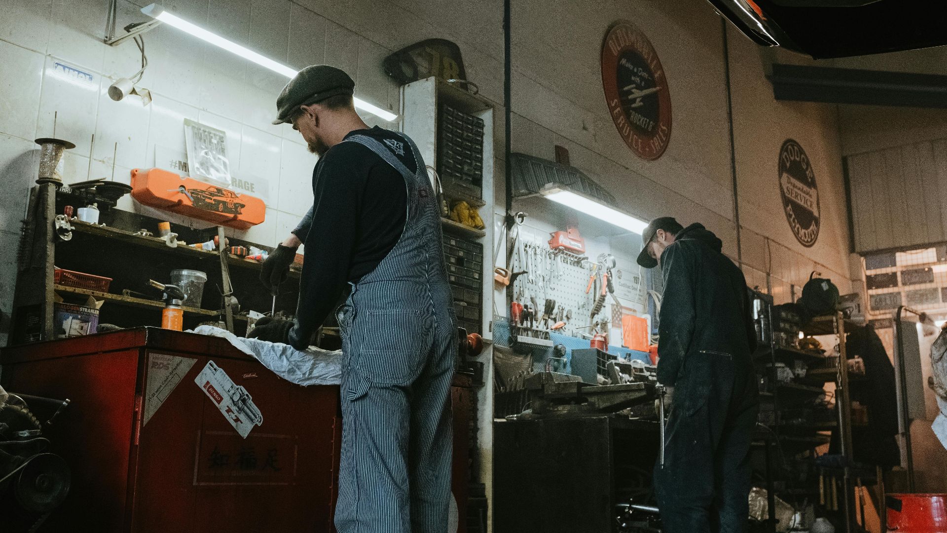 Two mechanics in a garage working on vehicle repair and maintenance.