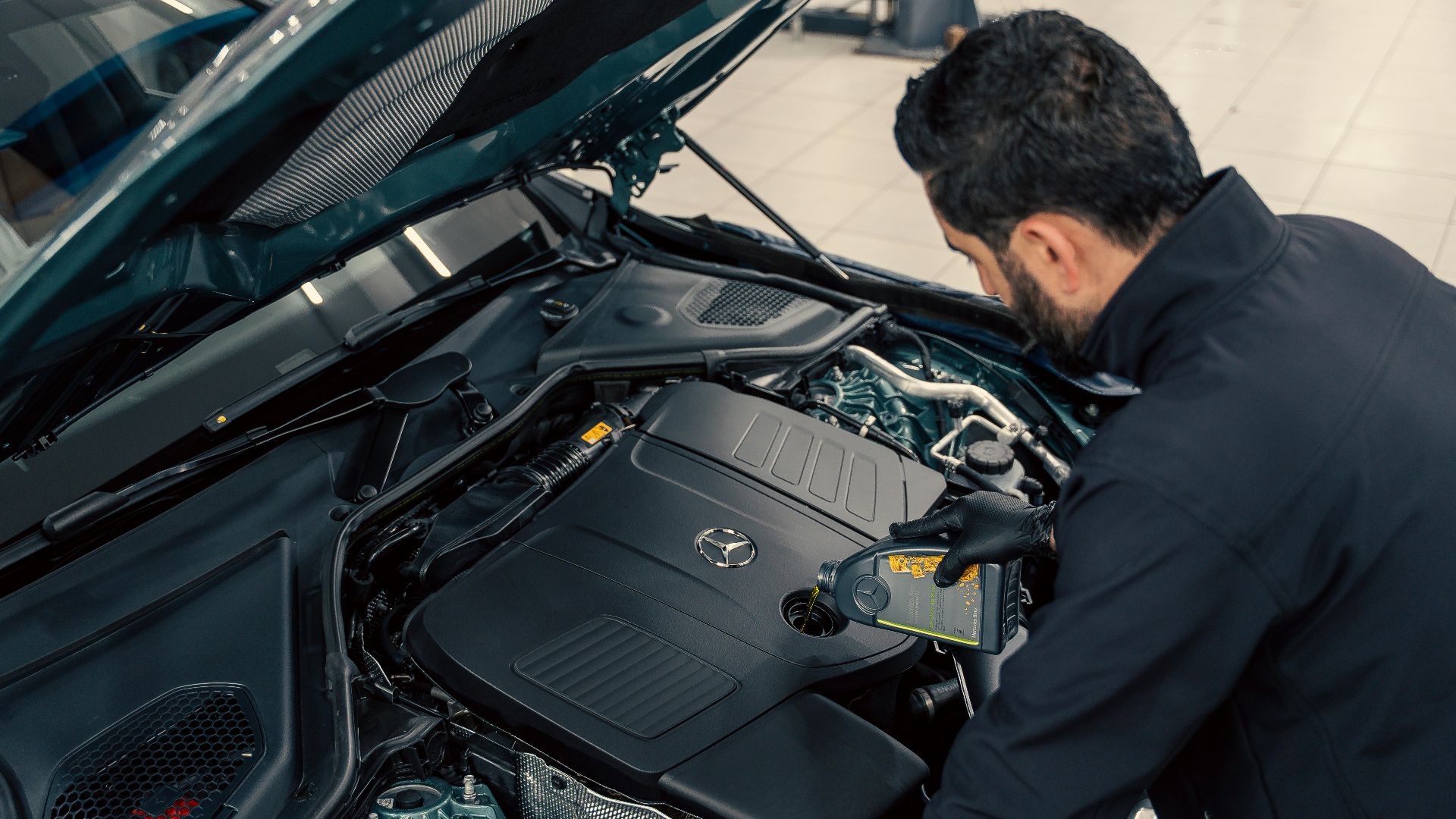 Mechanic inspecting and filling engine oil in a car at an indoor service center.