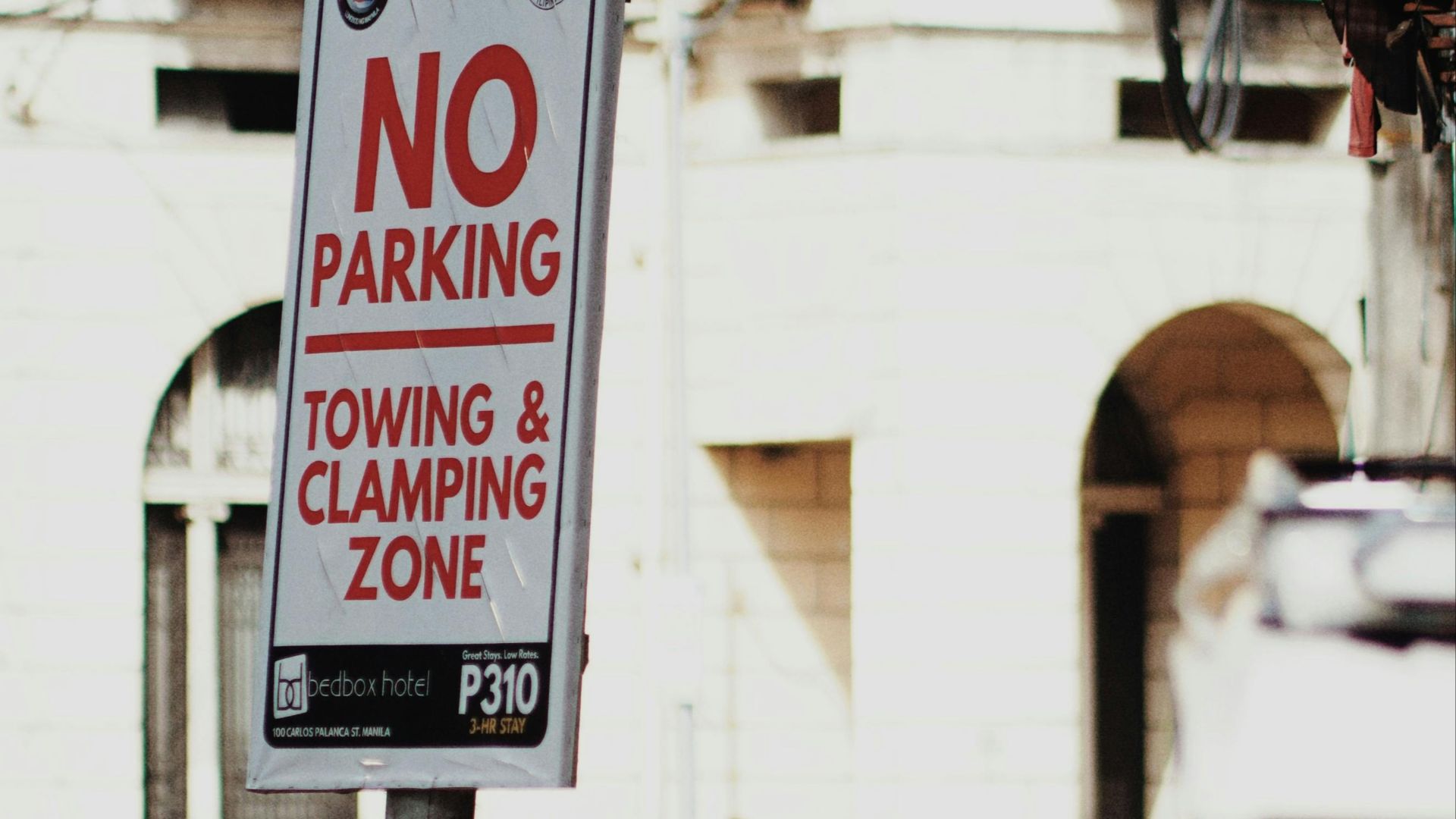 A woman stands on a city street near a no parking sign and urban buildings.