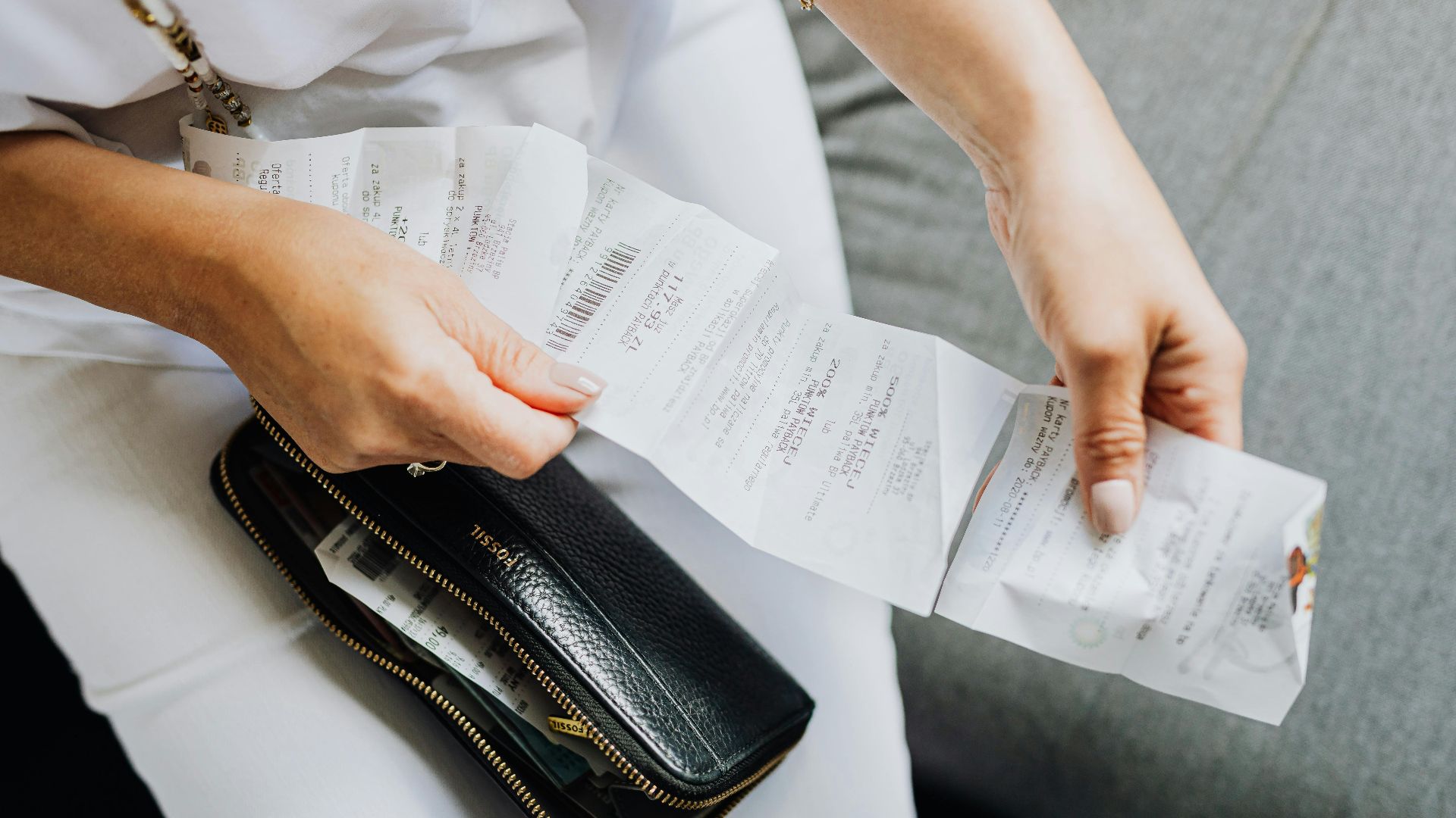 Close-up of a woman's hands managing multiple receipts taken from a black wallet.