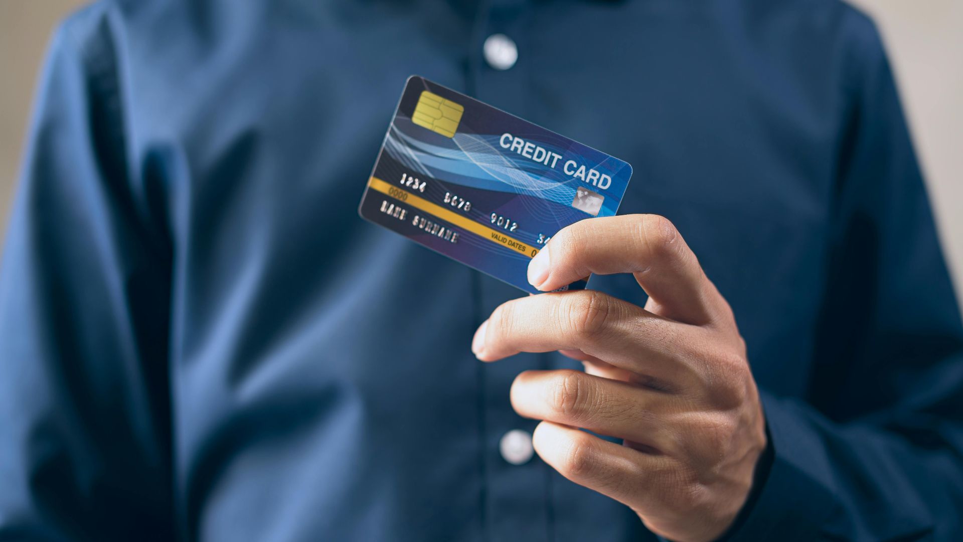 Close-up of a person holding a credit card in a hand, wearing a button-up shirt.