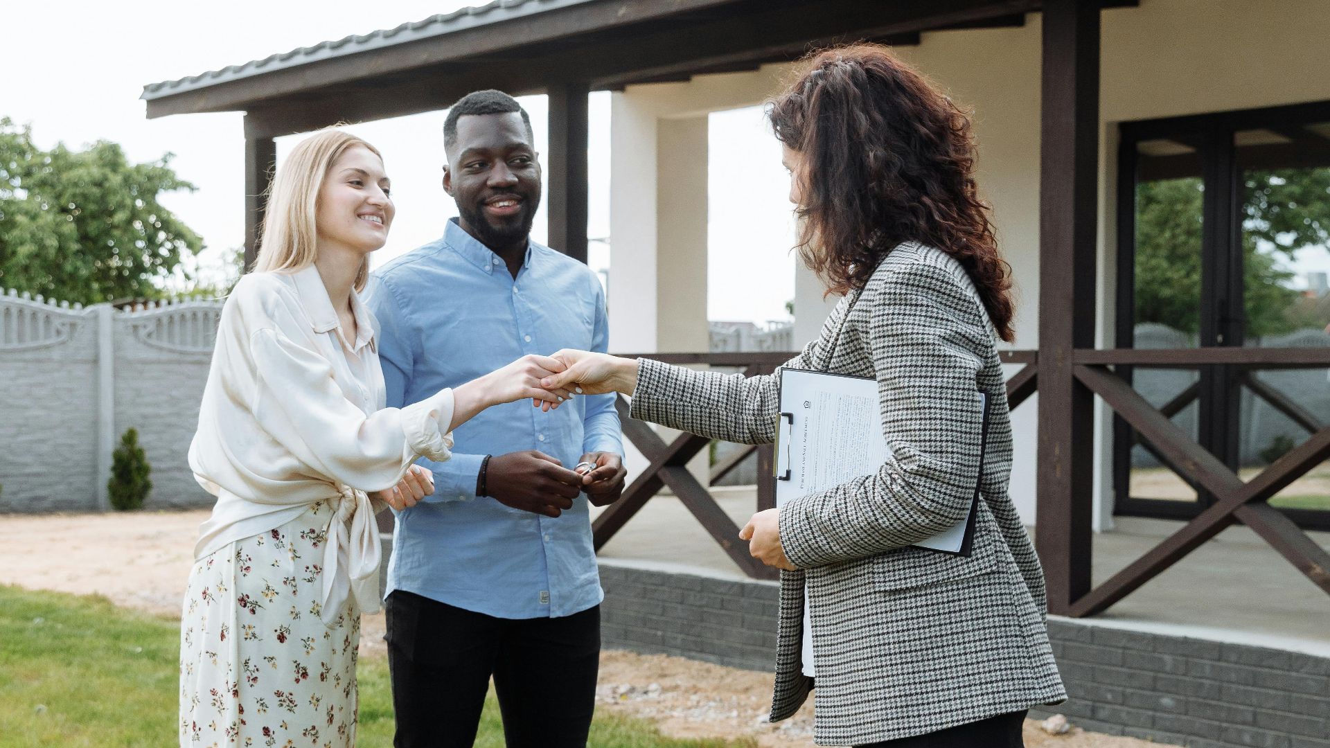 A realtor finalizes a home sale with a handshake agreement, welcoming new homeowners to their property.