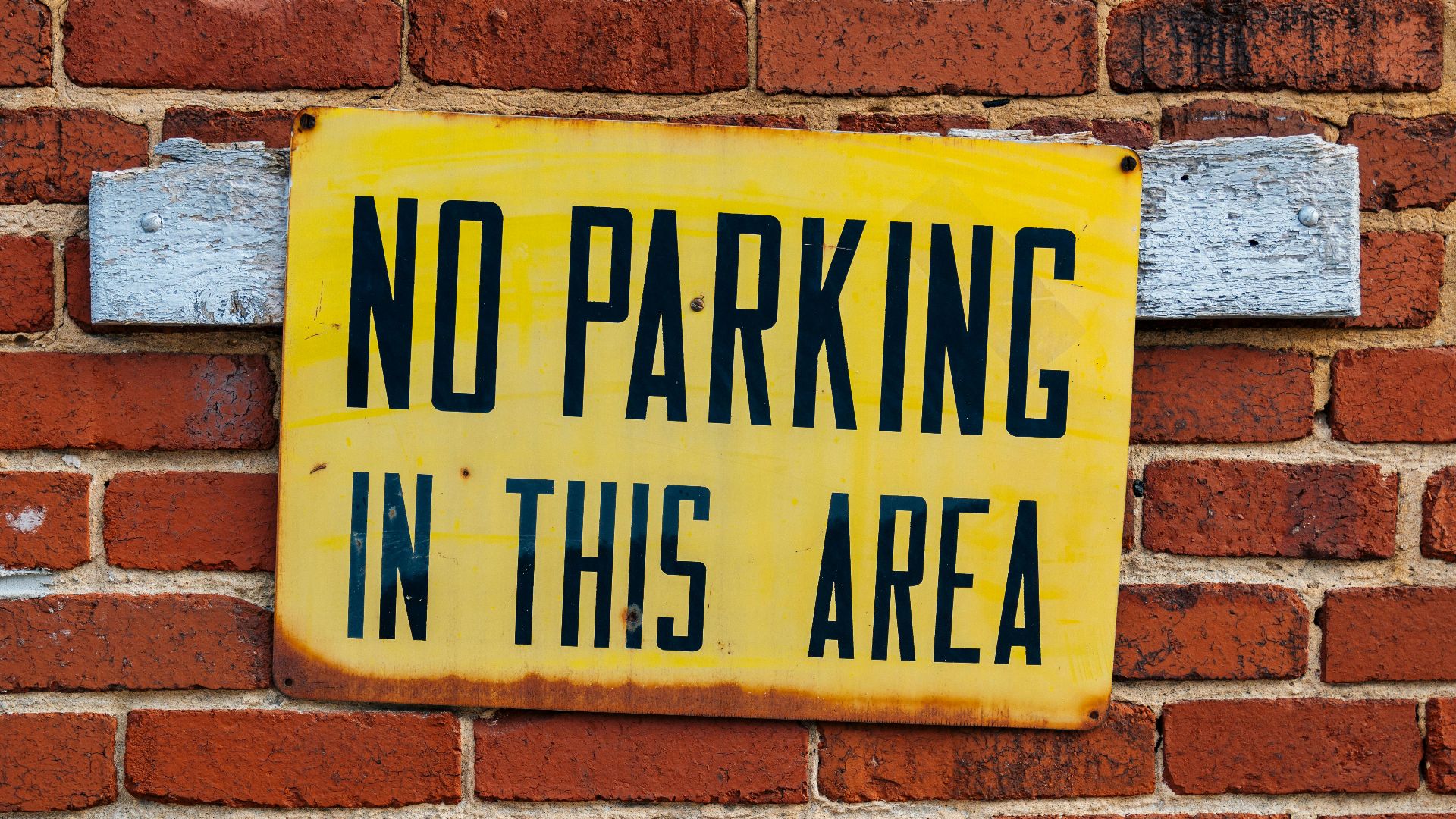 Bright yellow no parking sign attached to a red brick wall.