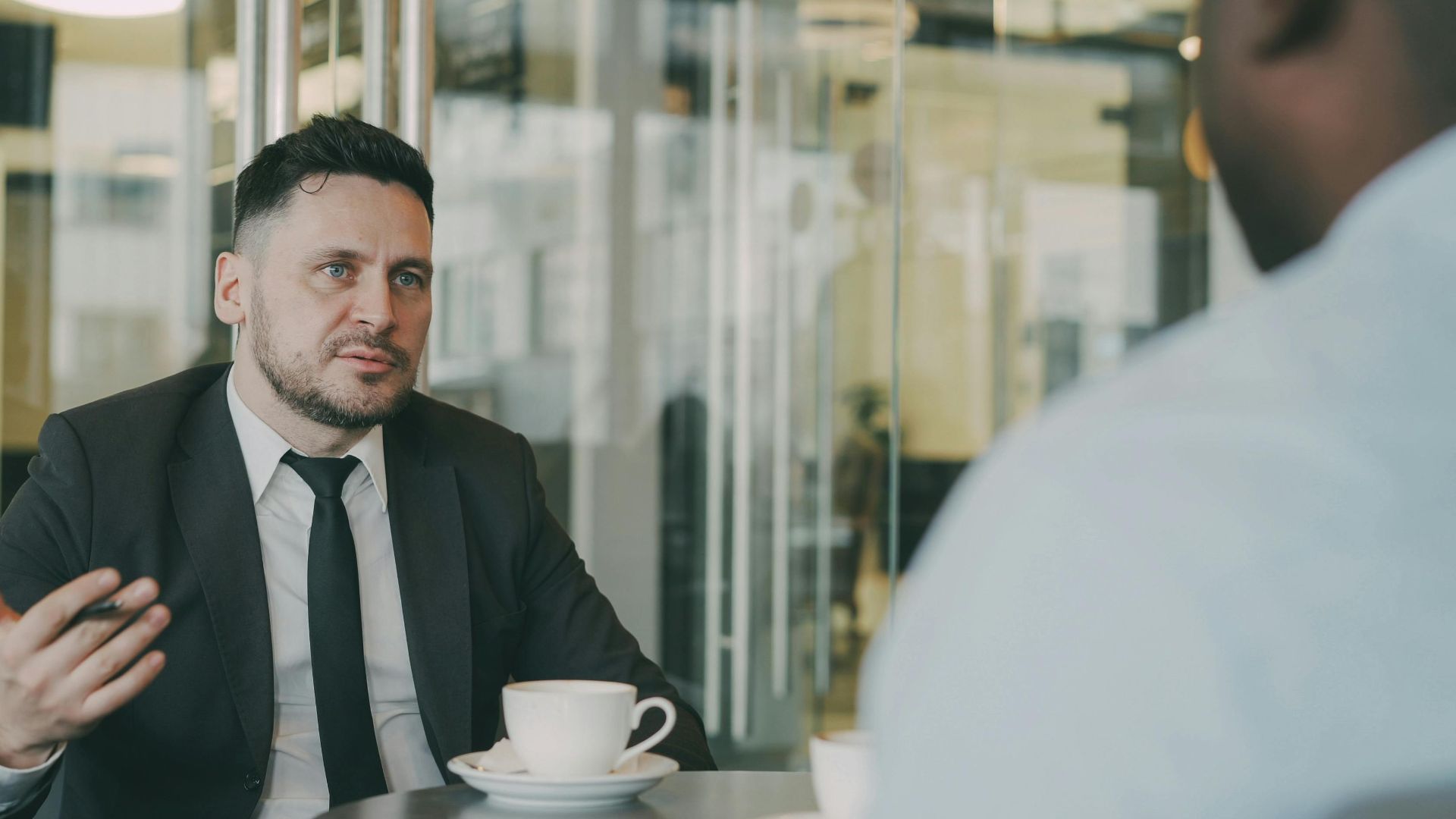 Two businessmen having a professional discussion over coffee in a modern cafe setting.