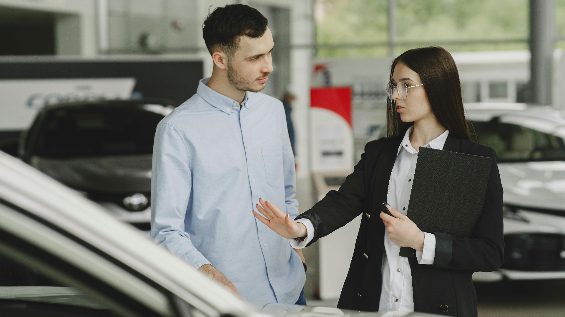A salesperson and customer discussing car features in a dealership setting.