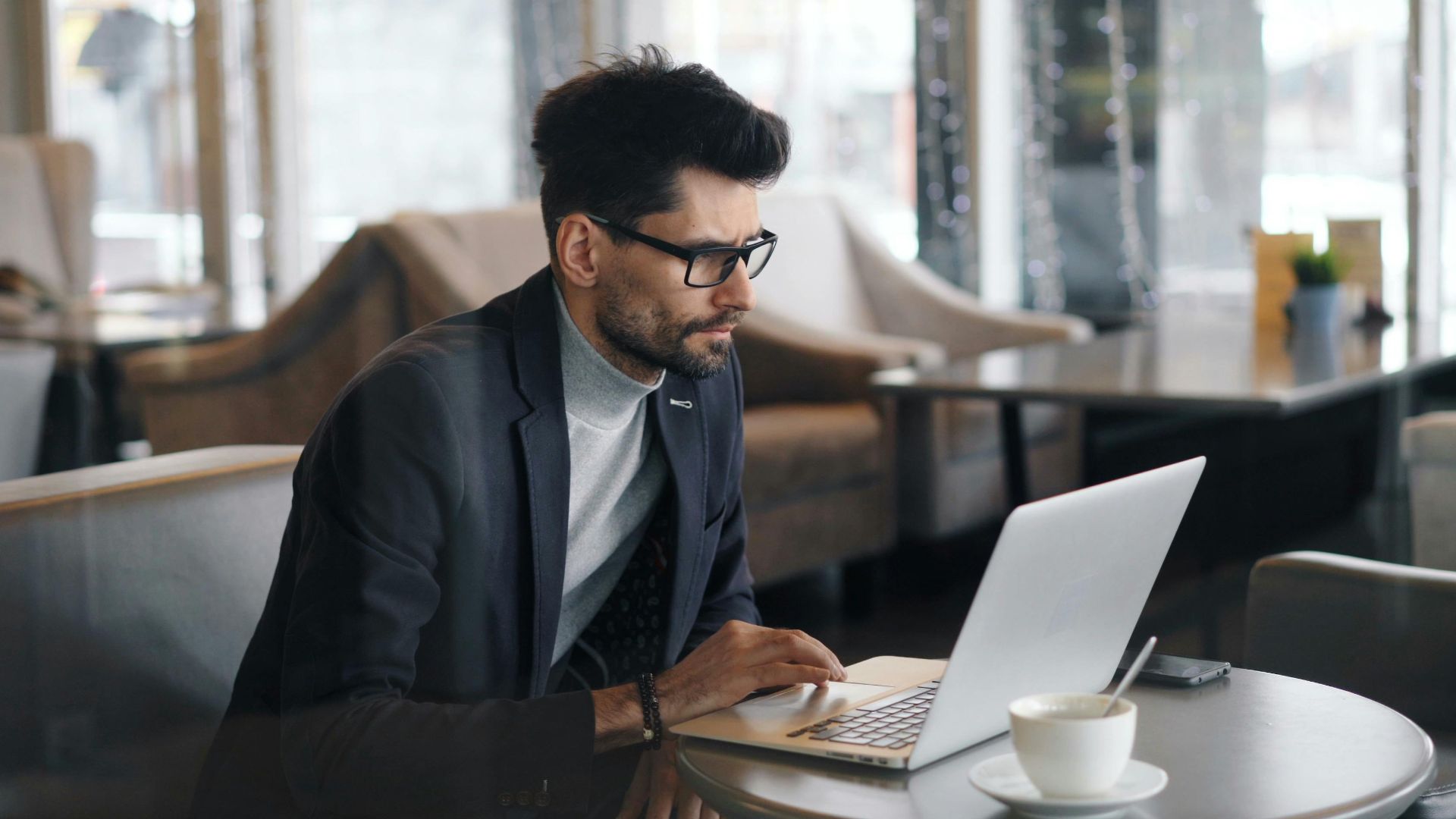Focused businessman working on a laptop in a stylish café, drinking coffee.
