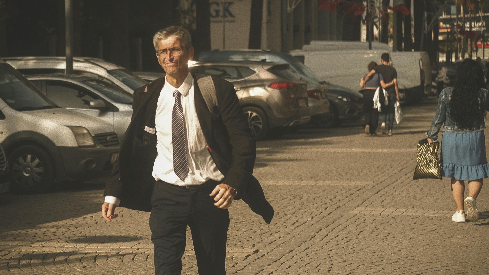 Senior man in suit confidently walks down a sunny city street.