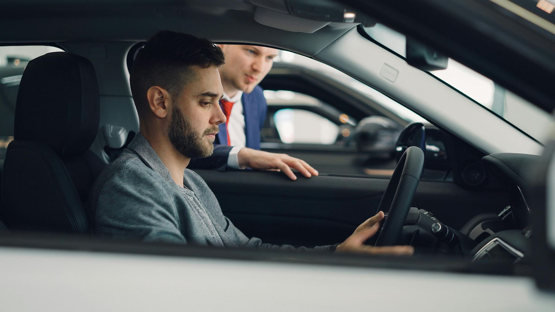 Man examining car interior with salesman at a dealership, highlighting car features.