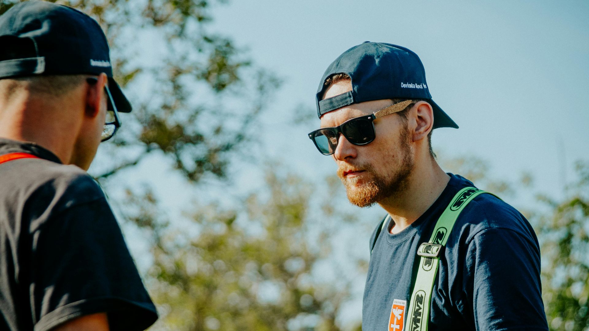 Two men in casual attire conversing outdoors on a sunny day.