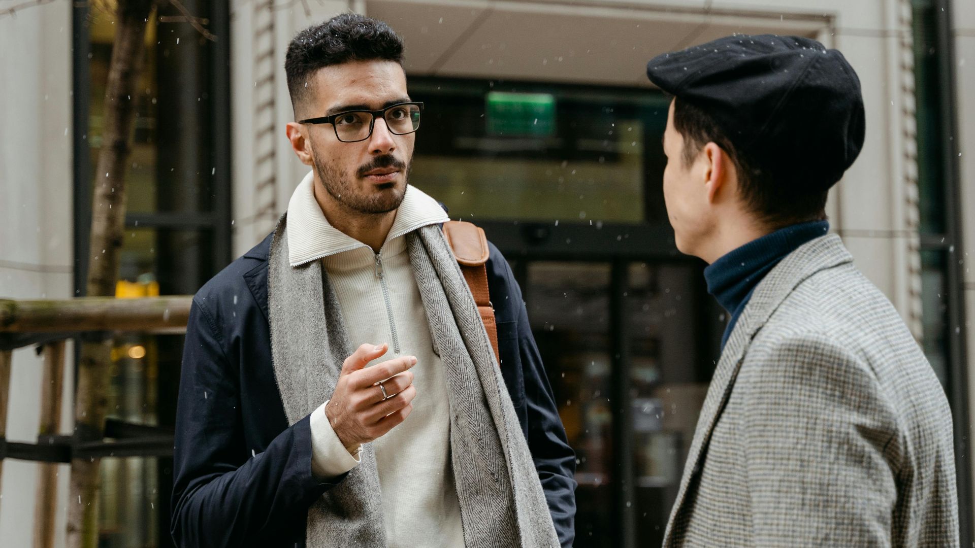 Two businessmen engaged in conversation outside in winter attire with snow falling lightly.