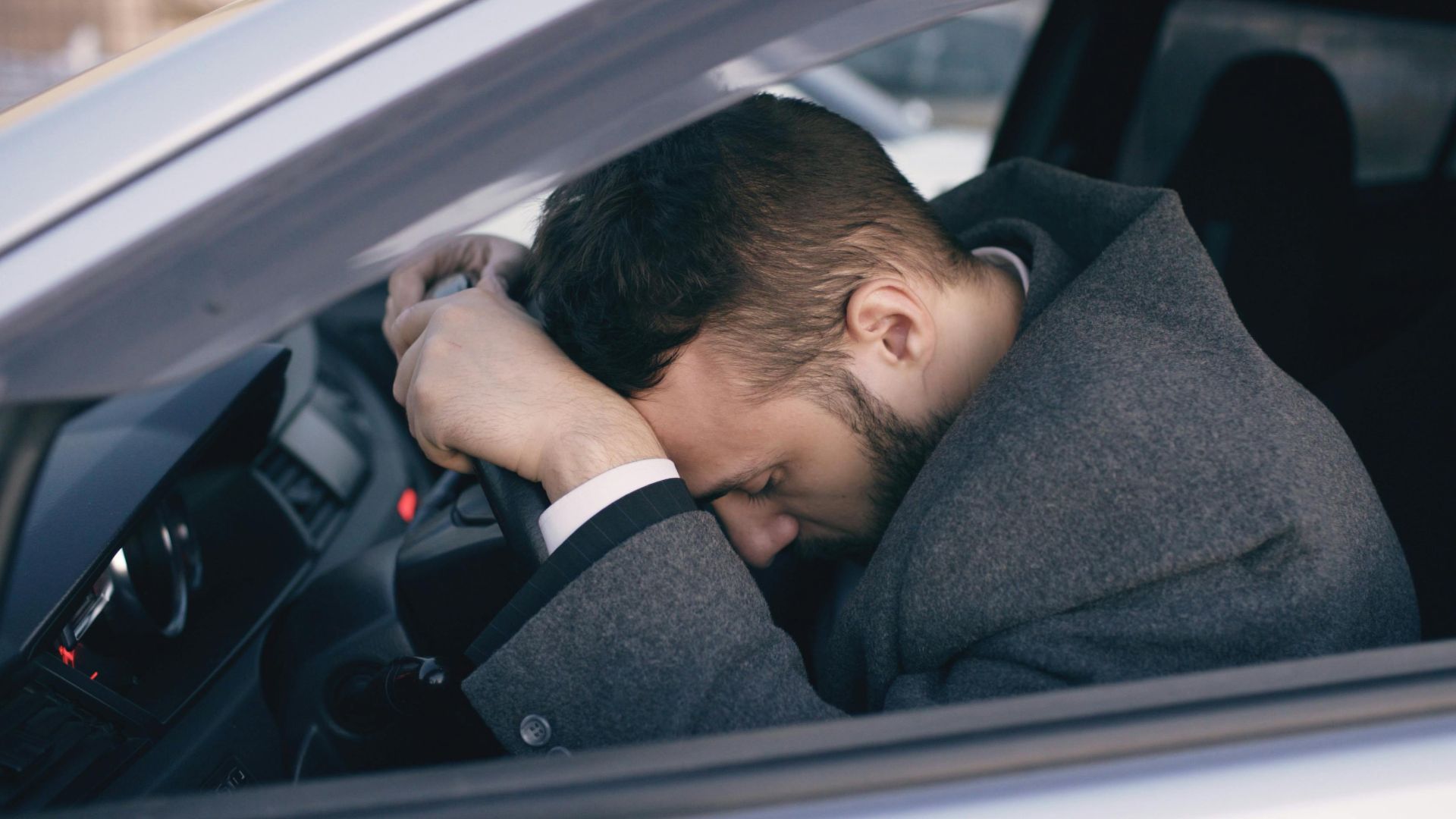 Man in car showing stress with head on steering wheel, highlighting emotional fatigue.
