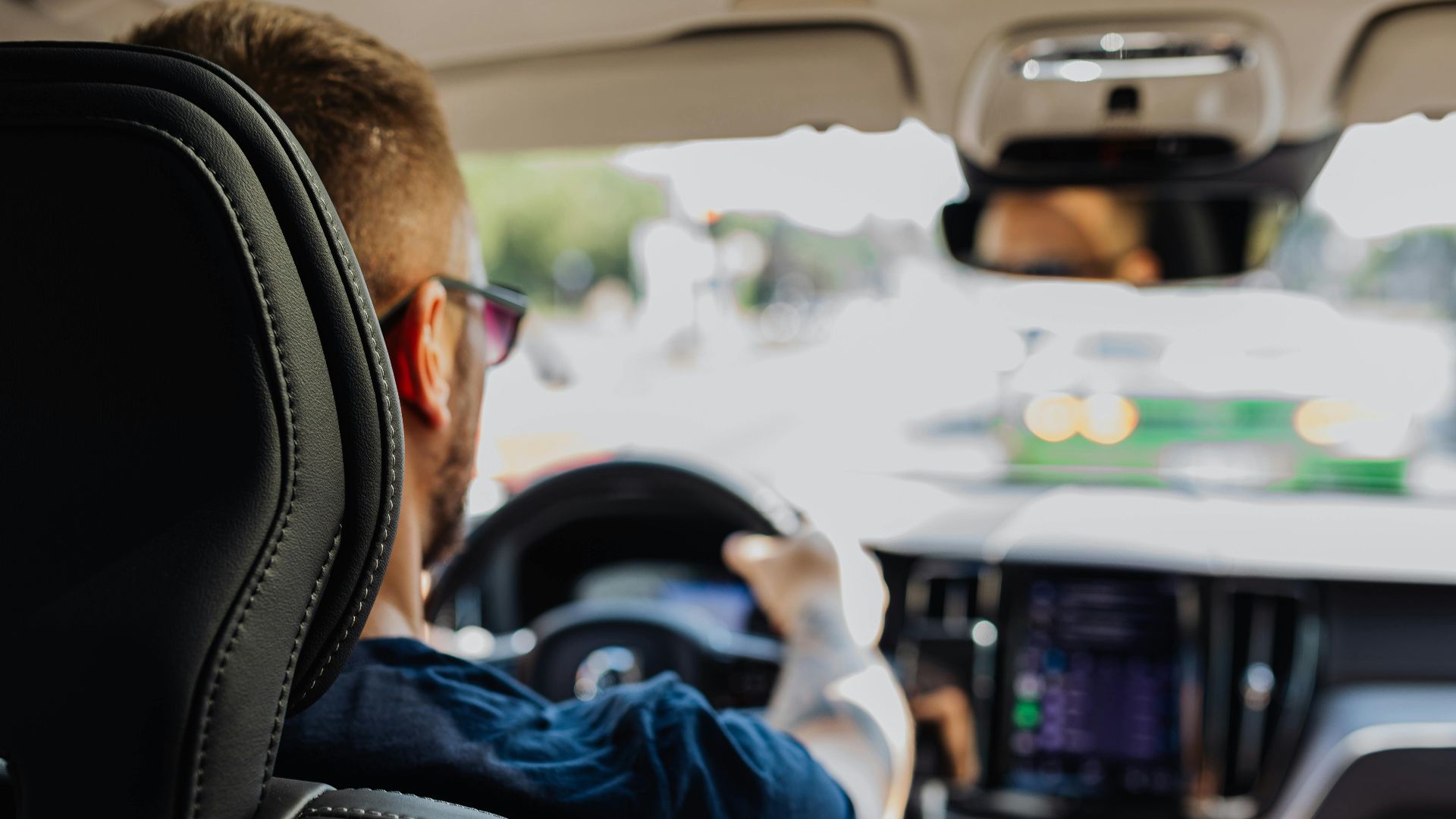 Close-up of a man driving a modern vehicle from behind with a blurred urban background.