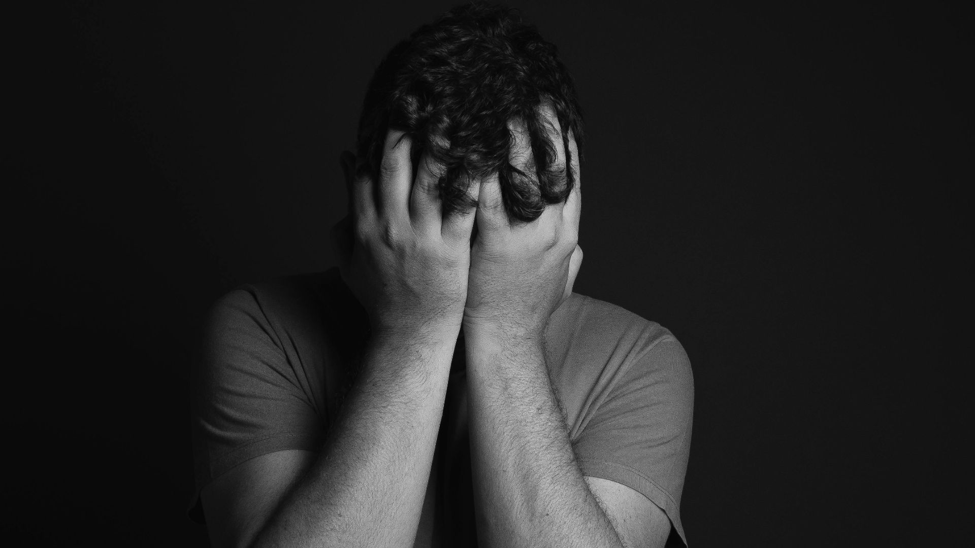 A grayscale portrait of a man covering his face, depicting emotion and mental health themes.