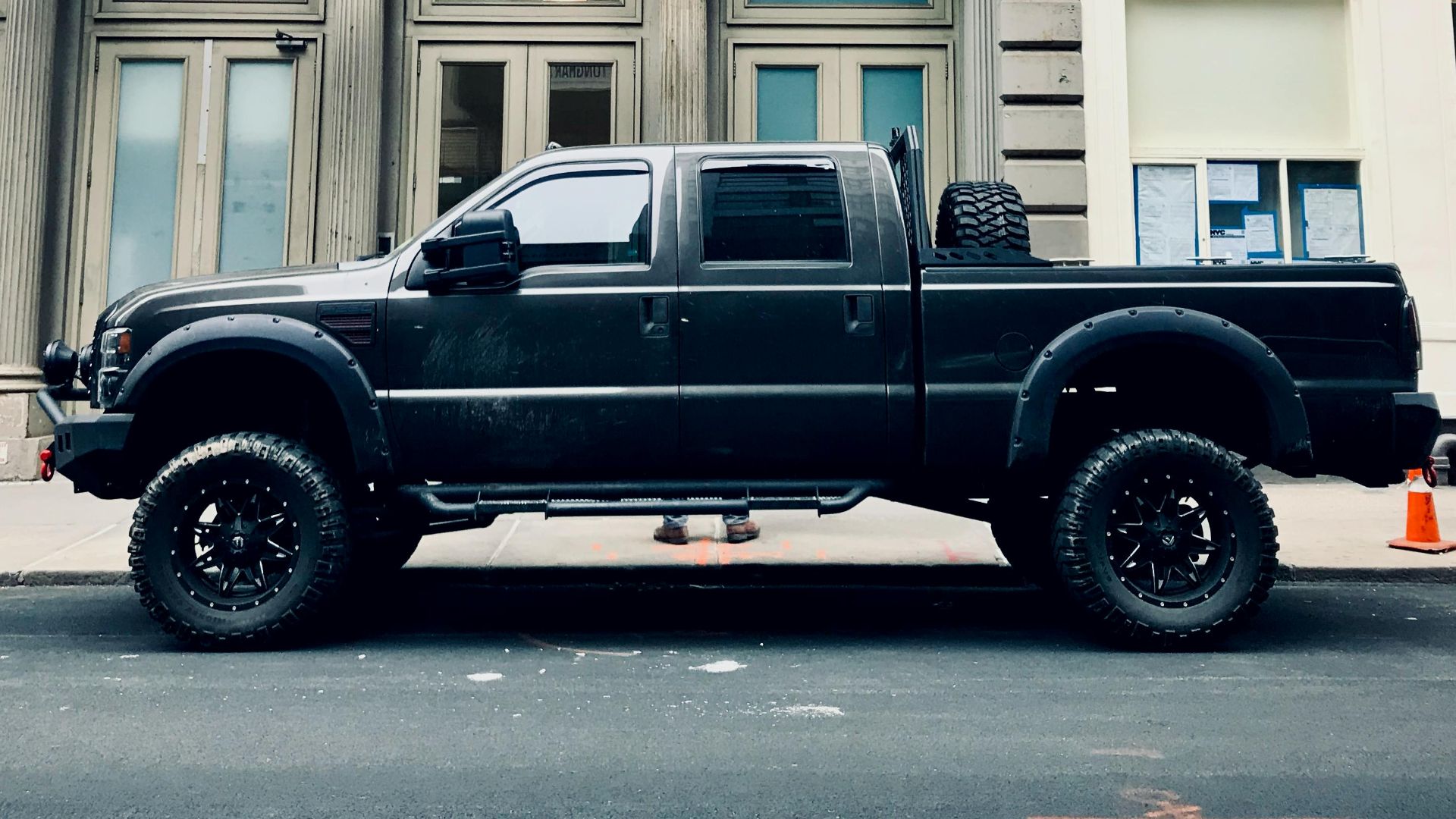 Black pickup truck parked in front of urban building, showcasing rugged design and tires.