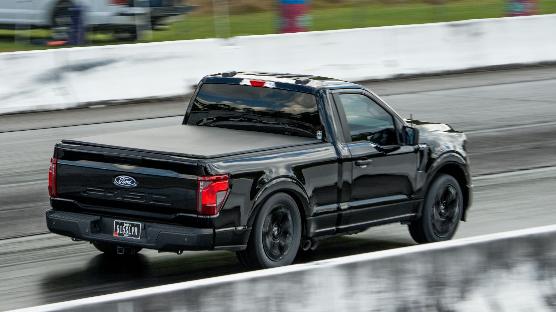 Black pickup truck speeding on an outdoor race track, showcasing motion and speed.