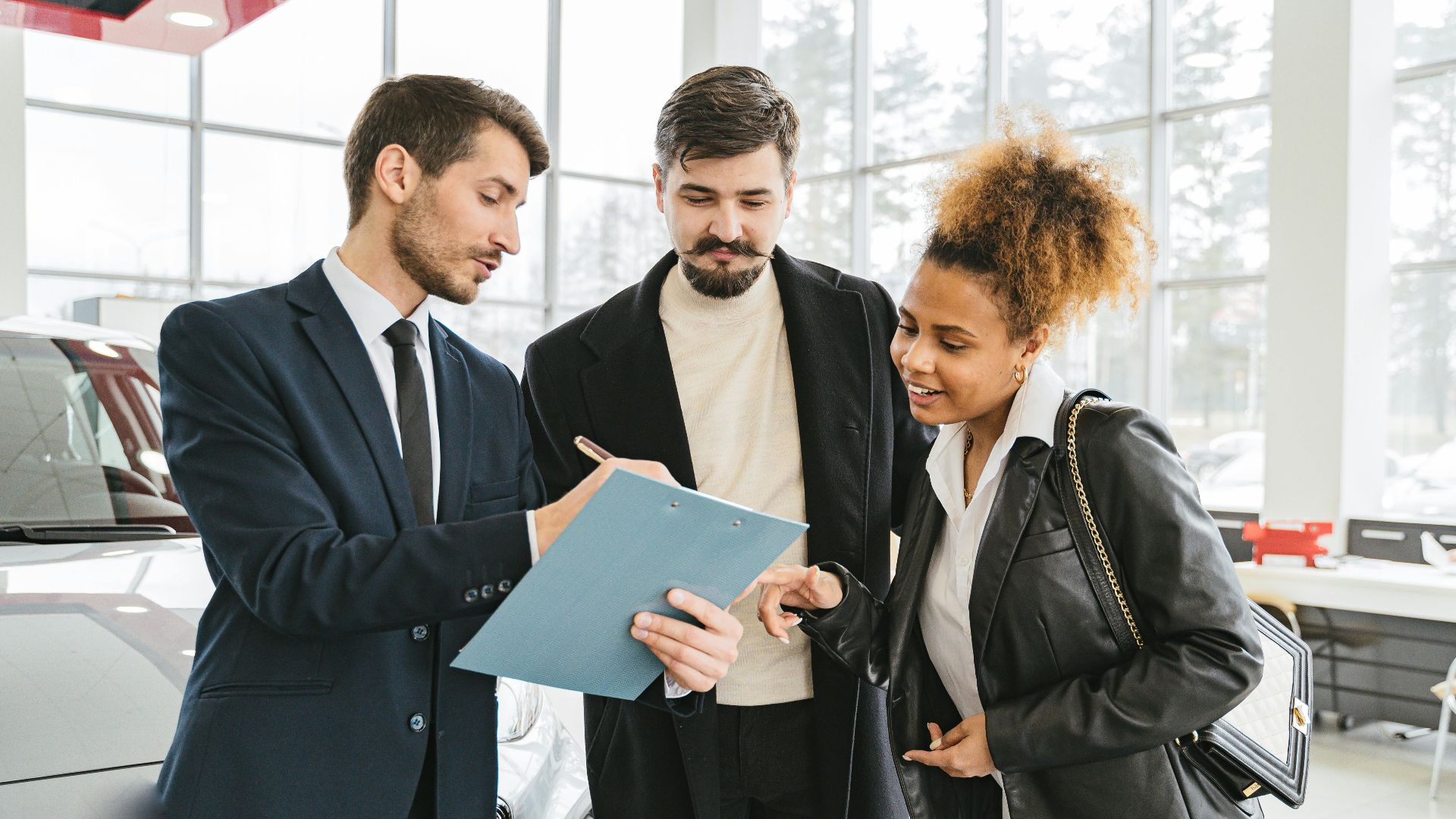 Three business professionals discussing car purchase details inside a modern dealership.
