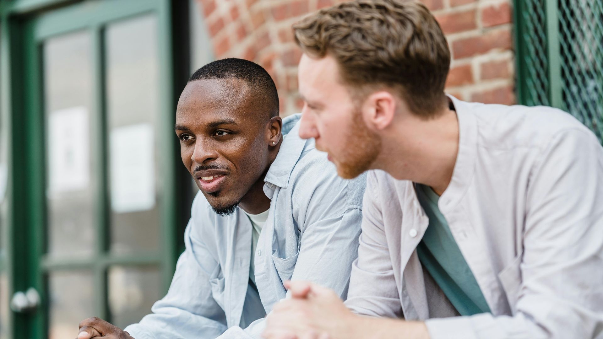 Two young men chatting and smiling while leaning on a railing outdoors.