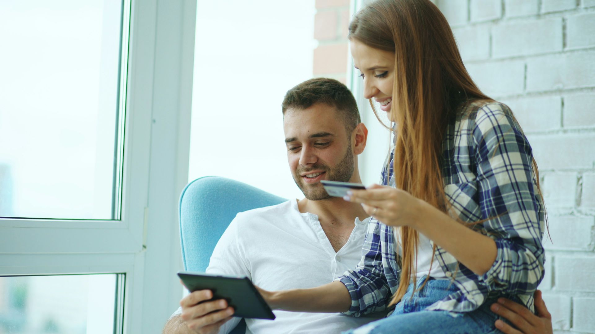 Couple happily shopping online with tablet and credit card.