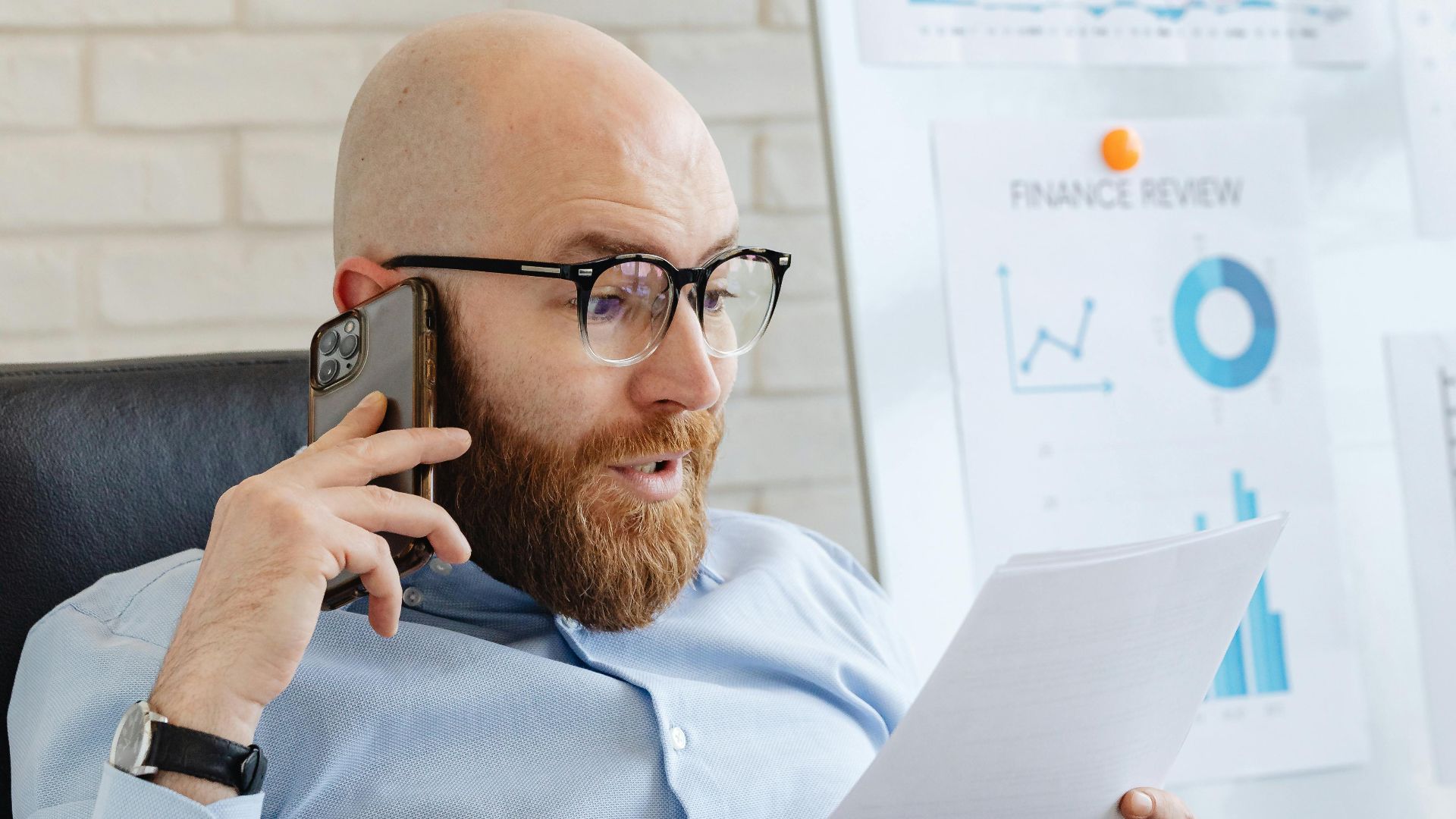 Professional analyzing data charts and graphs on paper and phone in office setting.