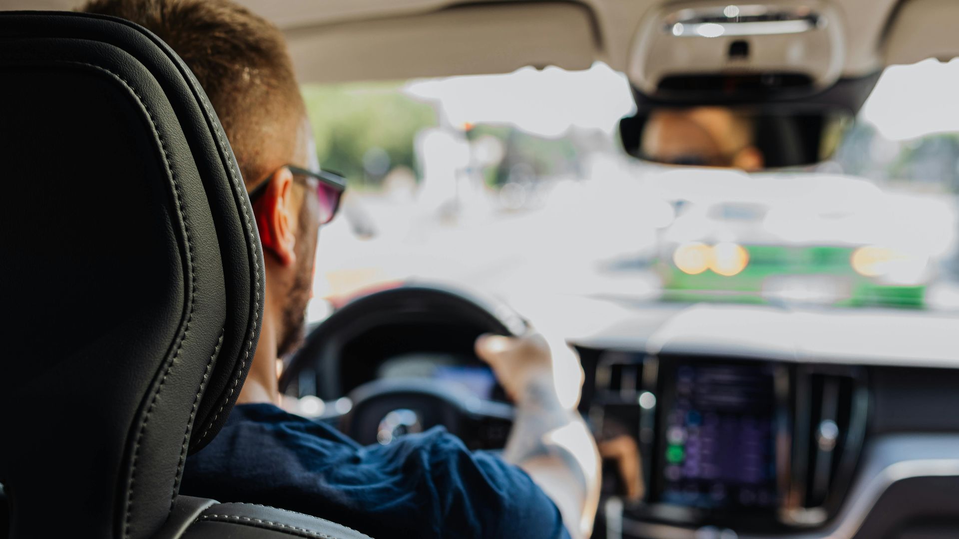 Close-up of a man driving a modern vehicle from behind with a blurred urban background.