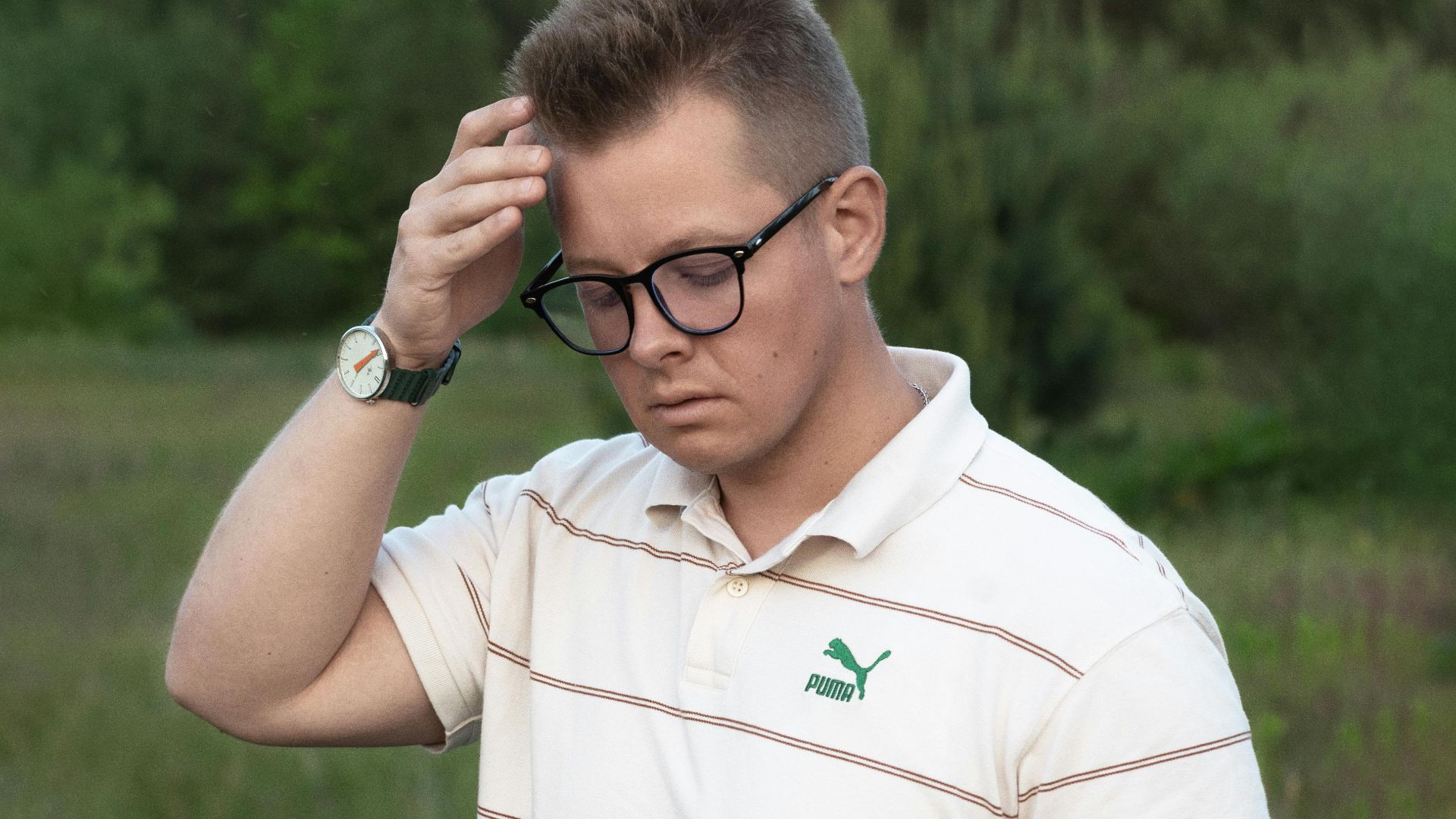 A young man in casual wear checking his smartphone in a natural outdoor setting, looking thoughtful.