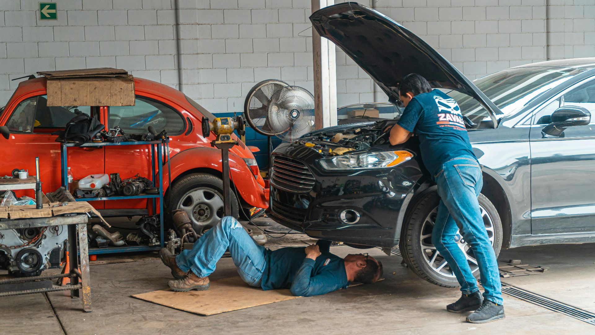 Mechanics working in an automotive workshop, repairing cars and performing maintenance.