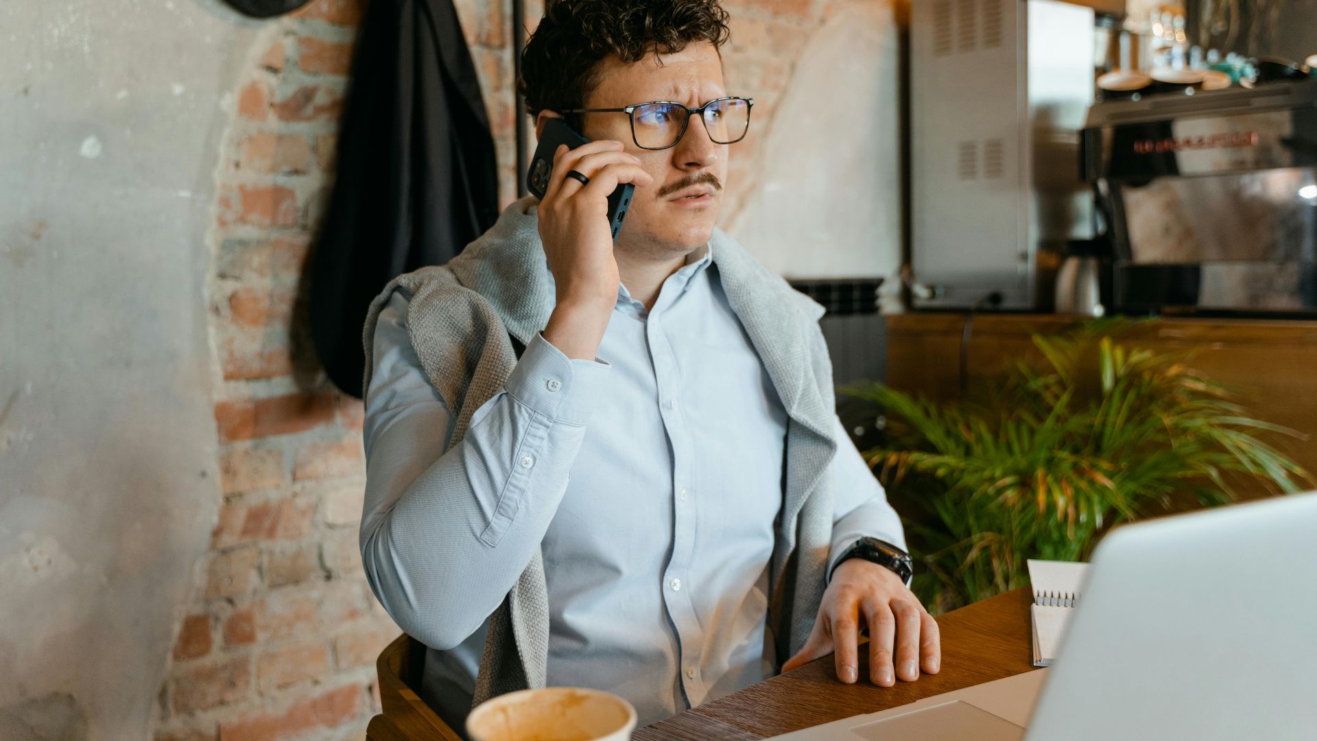 Man with glasses and mustache on a phone call in a cozy cafe.