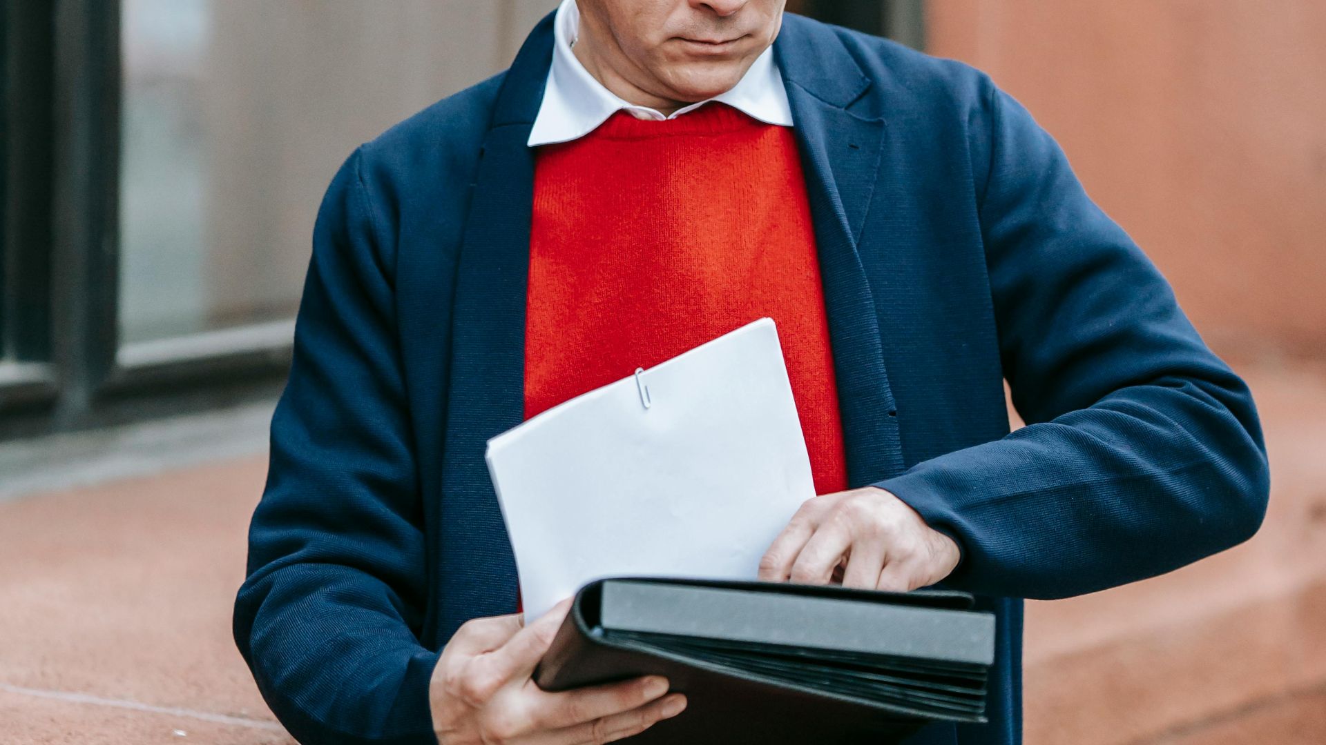 A man dressed in formal attire examines papers outside a building.
