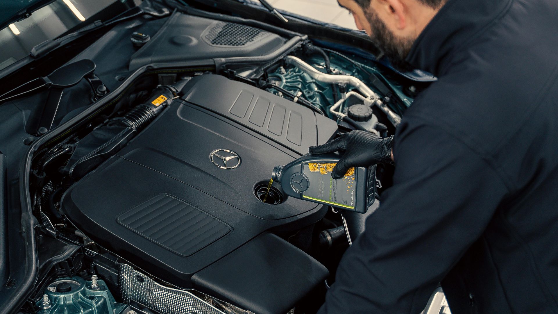 Mechanic inspecting and filling engine oil in a car at an indoor service center.