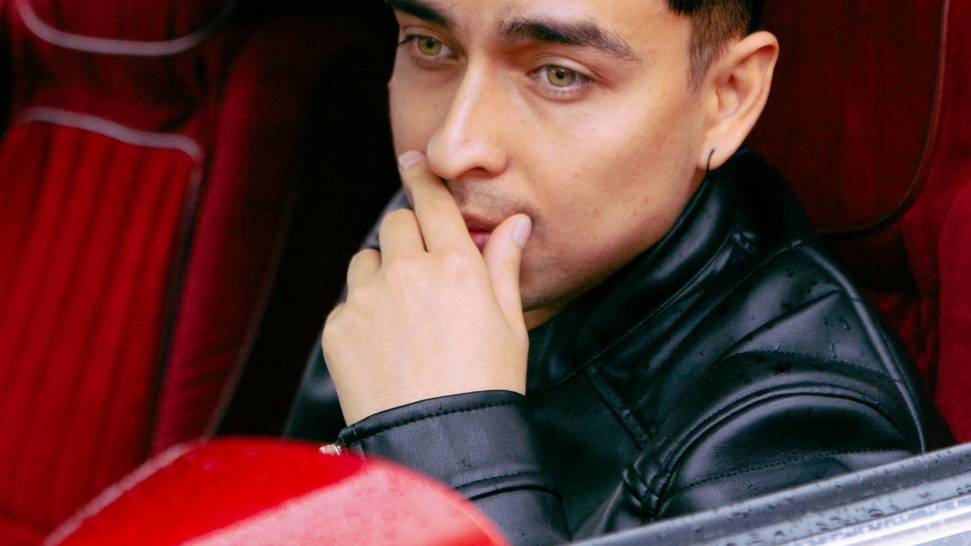 Thoughtful man in leather jacket sitting in car, lost in contemplation.