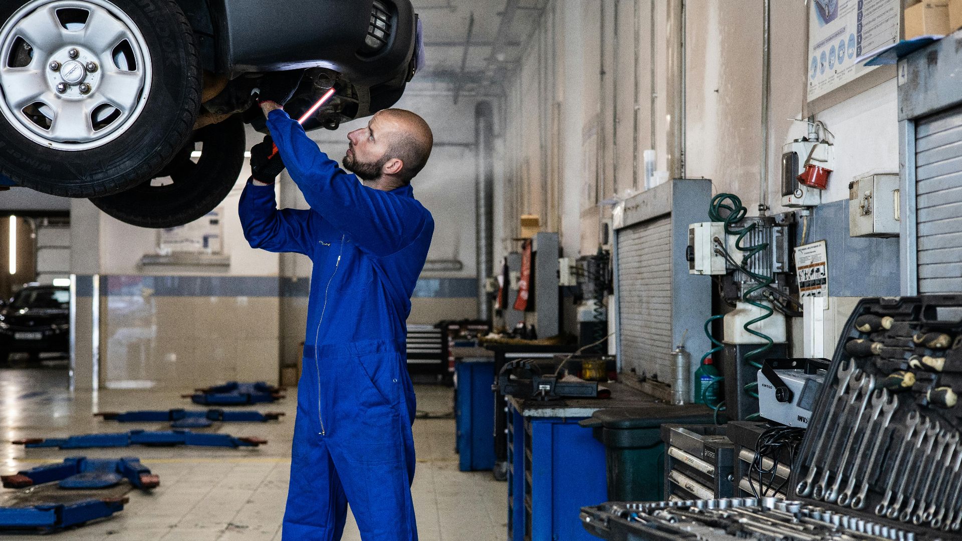 Mechanic inspecting a raised car in an auto workshop for maintenance and repair services.