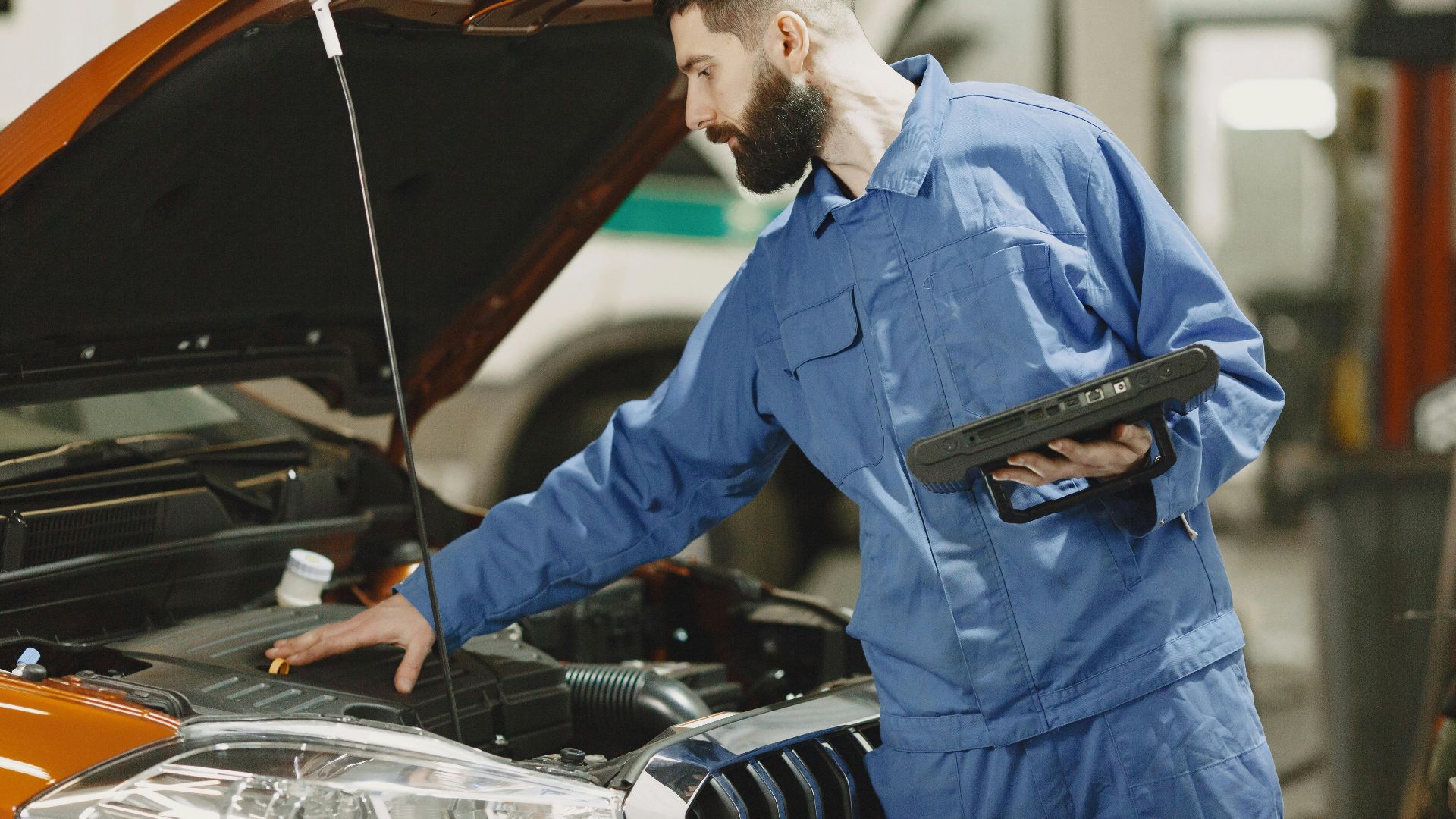 Professional mechanic examining a car engine under an open hood in a garage setting.