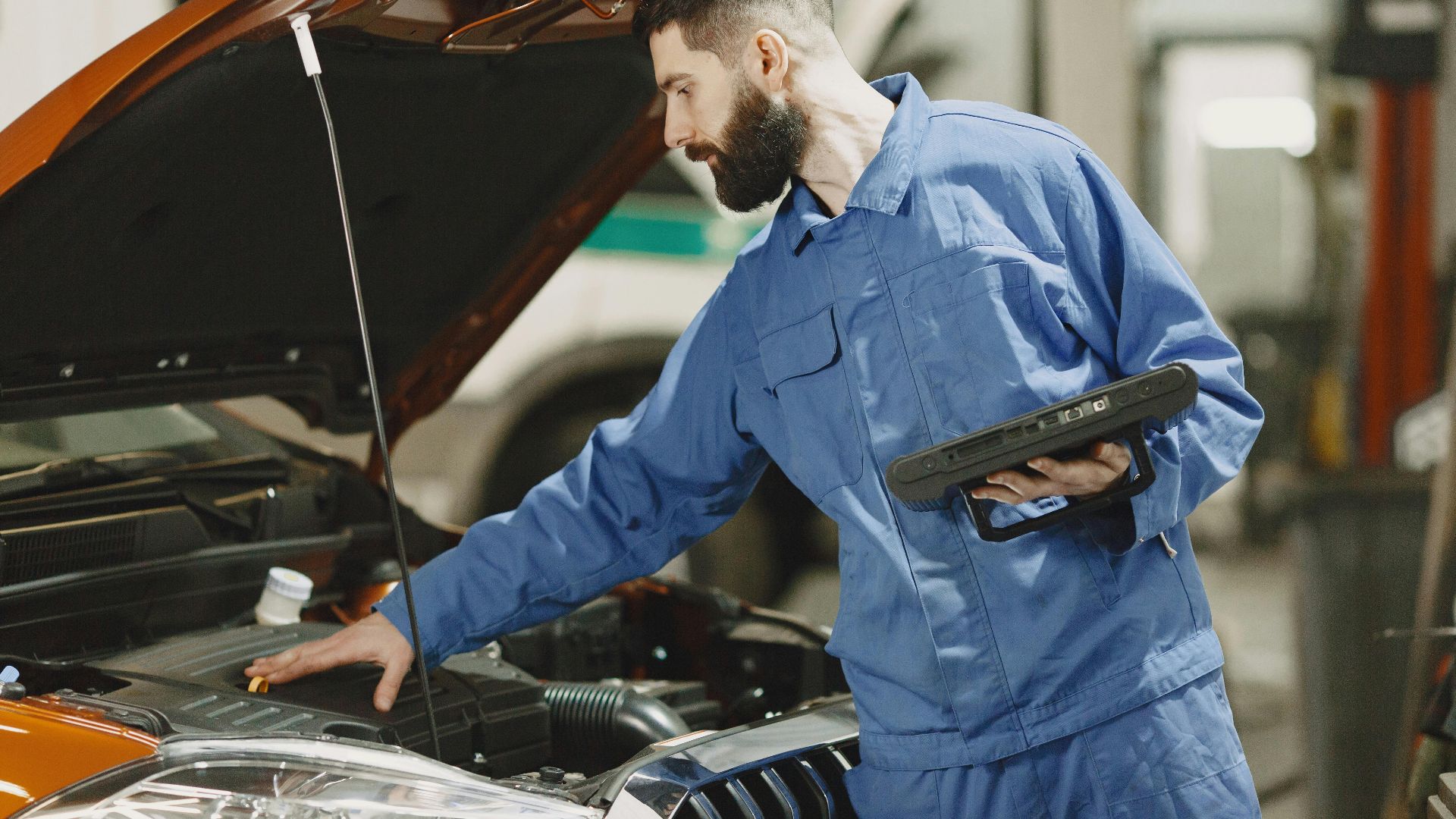 Professional mechanic examining a car engine under an open hood in a garage setting.