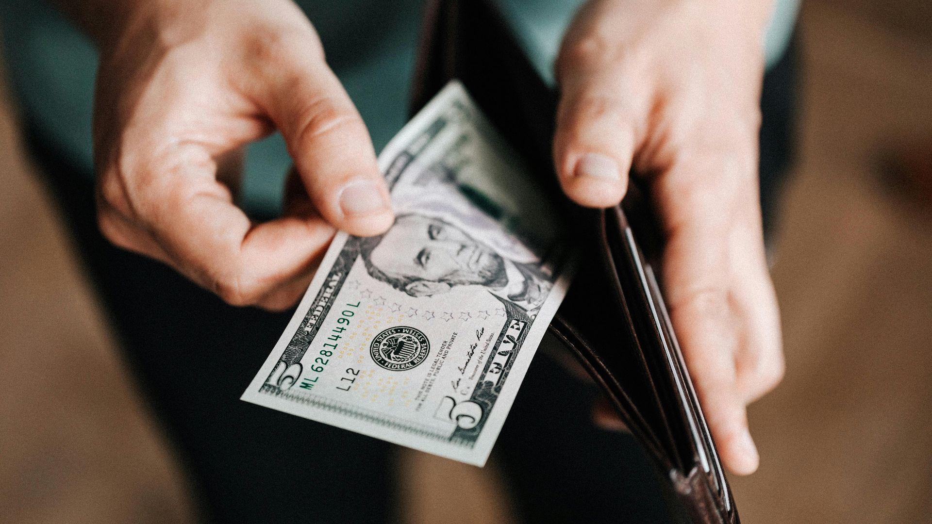Closeup of crop male in casual clothes taking dollars out of wallet while paying in shop