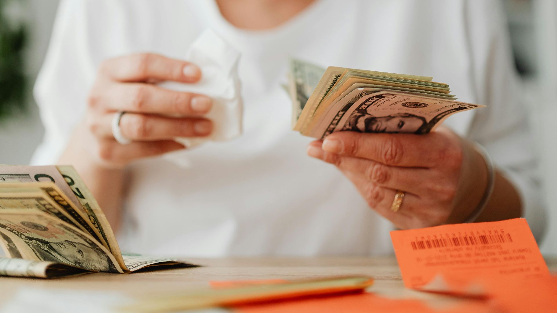 Woman emotionally managing finances at home, counting money and reviewing bills.