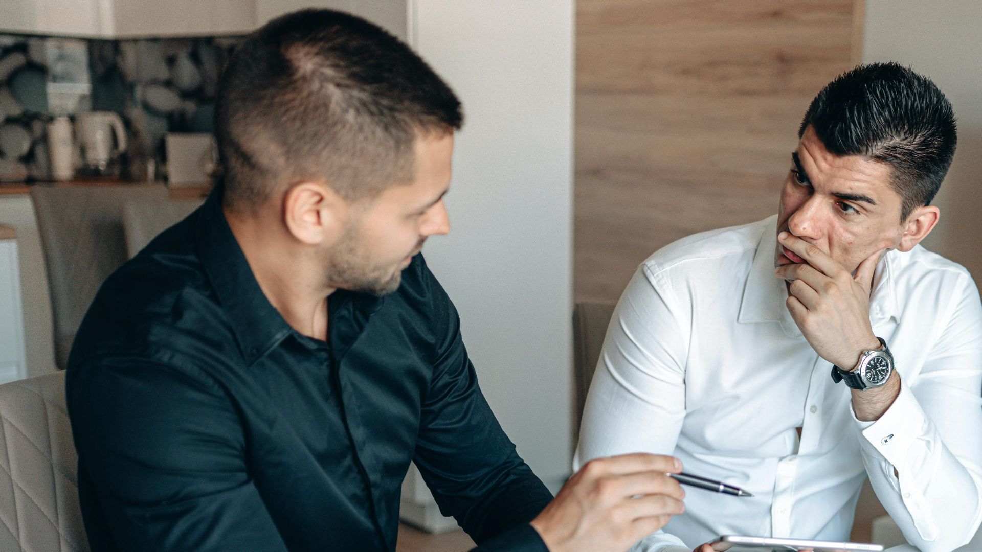 Two businessmen discussing stock market trends with trading screens in an office setting.