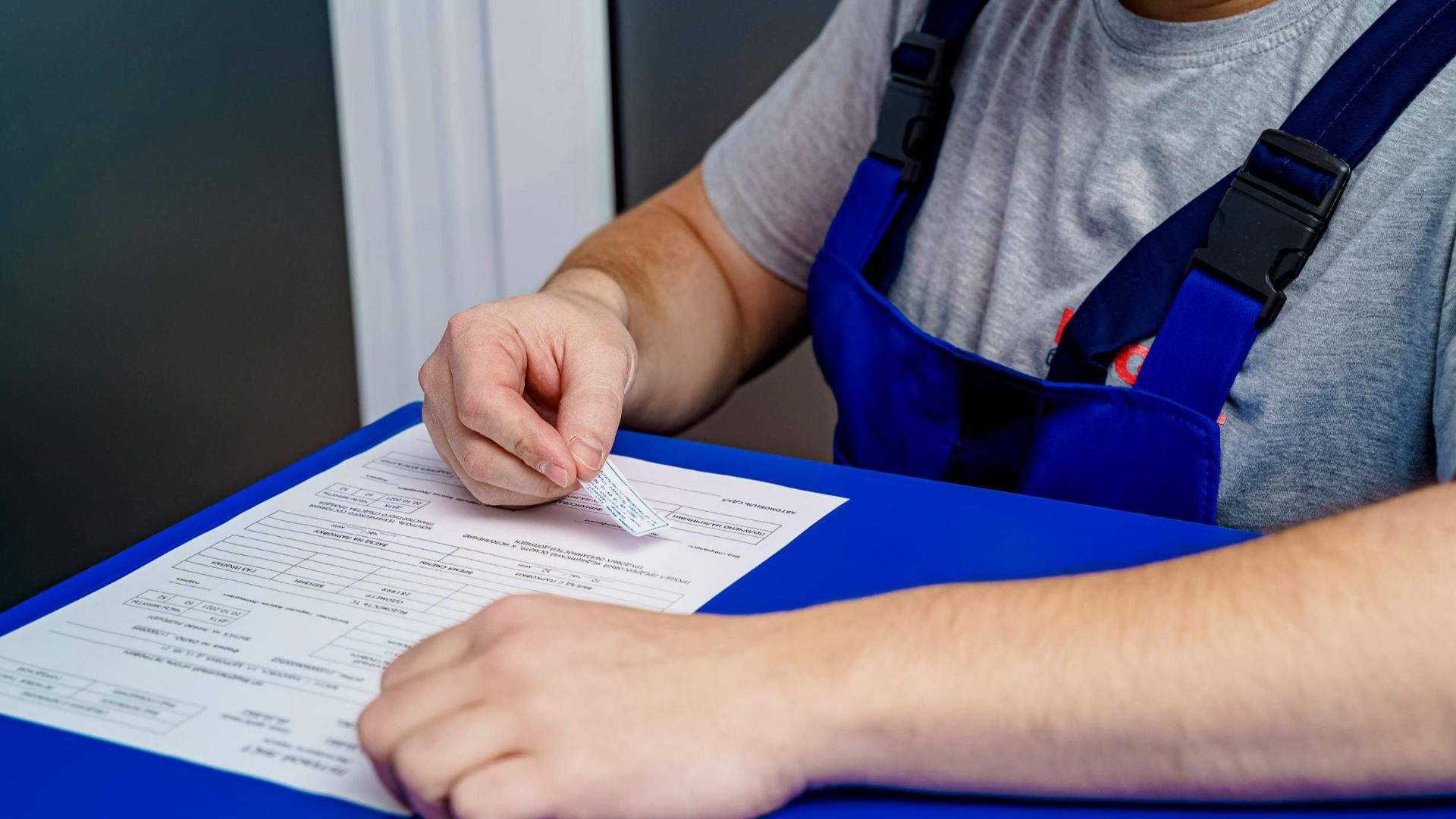 A mechanic in overalls reviews paperwork at a desk in an office setting.