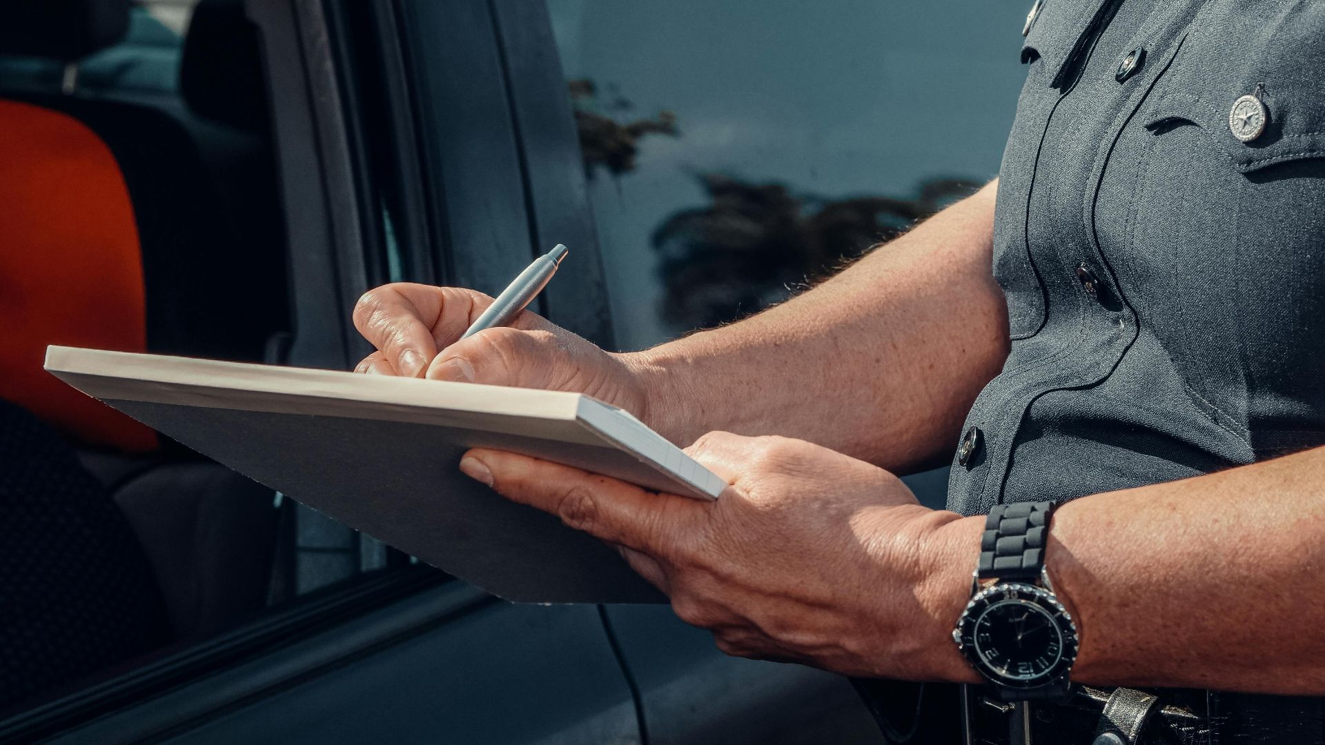 Close-up of a police officer writing a ticket by a car window. Law enforcement scene.