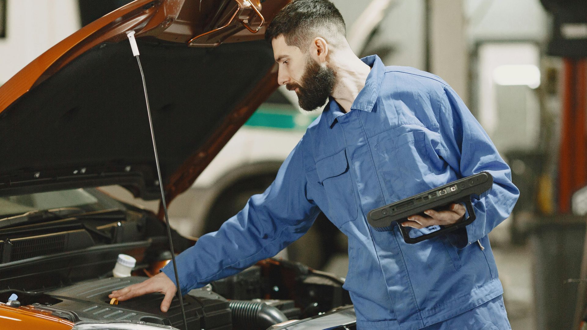 Professional mechanic examining a car engine under an open hood in a garage setting.