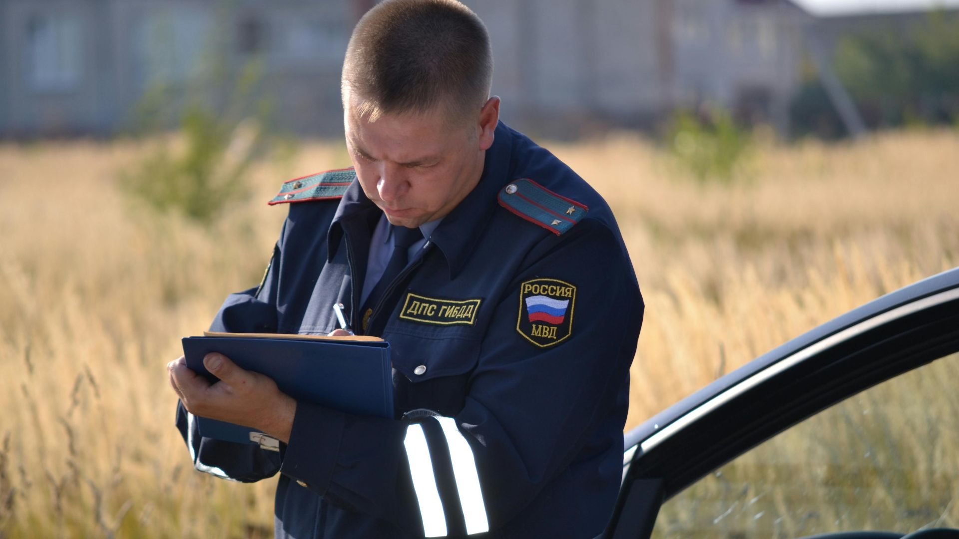 Police officer in uniform taking notes beside a car in a field.