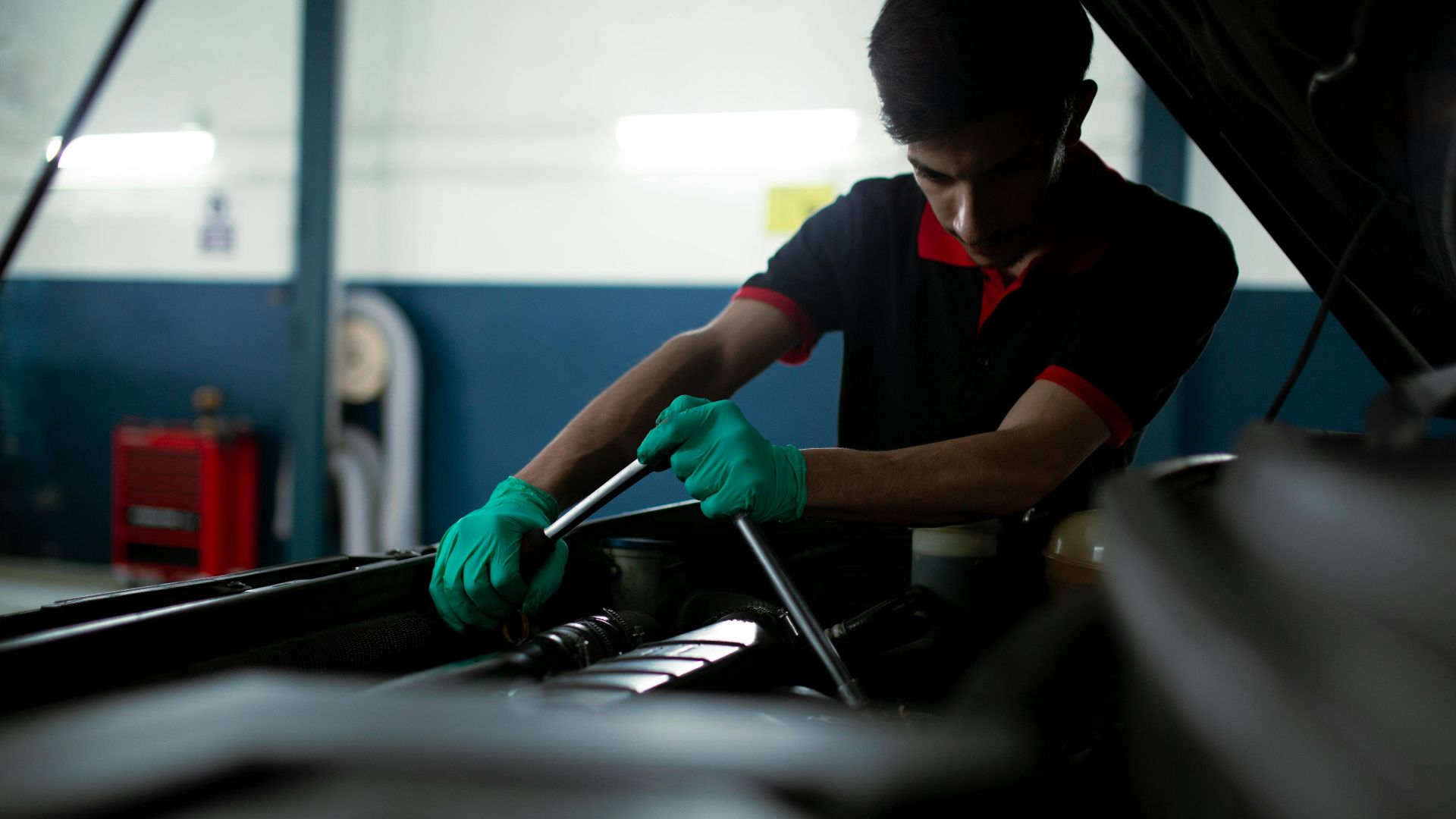 Mechanic wearing gloves using a torque wrench to repair a car engine in an indoor garage.