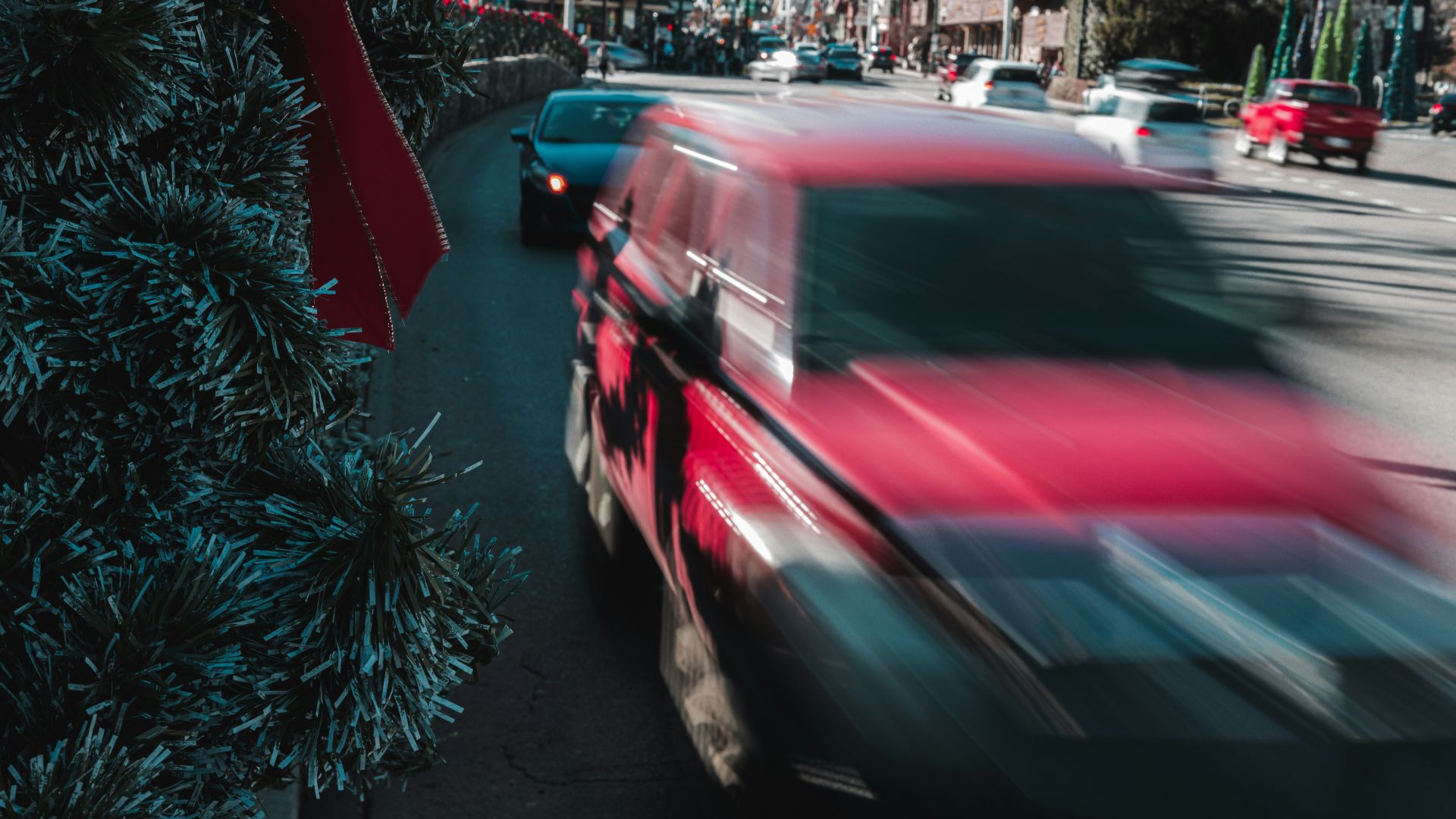 a red car driving down a street next to a christmas tree